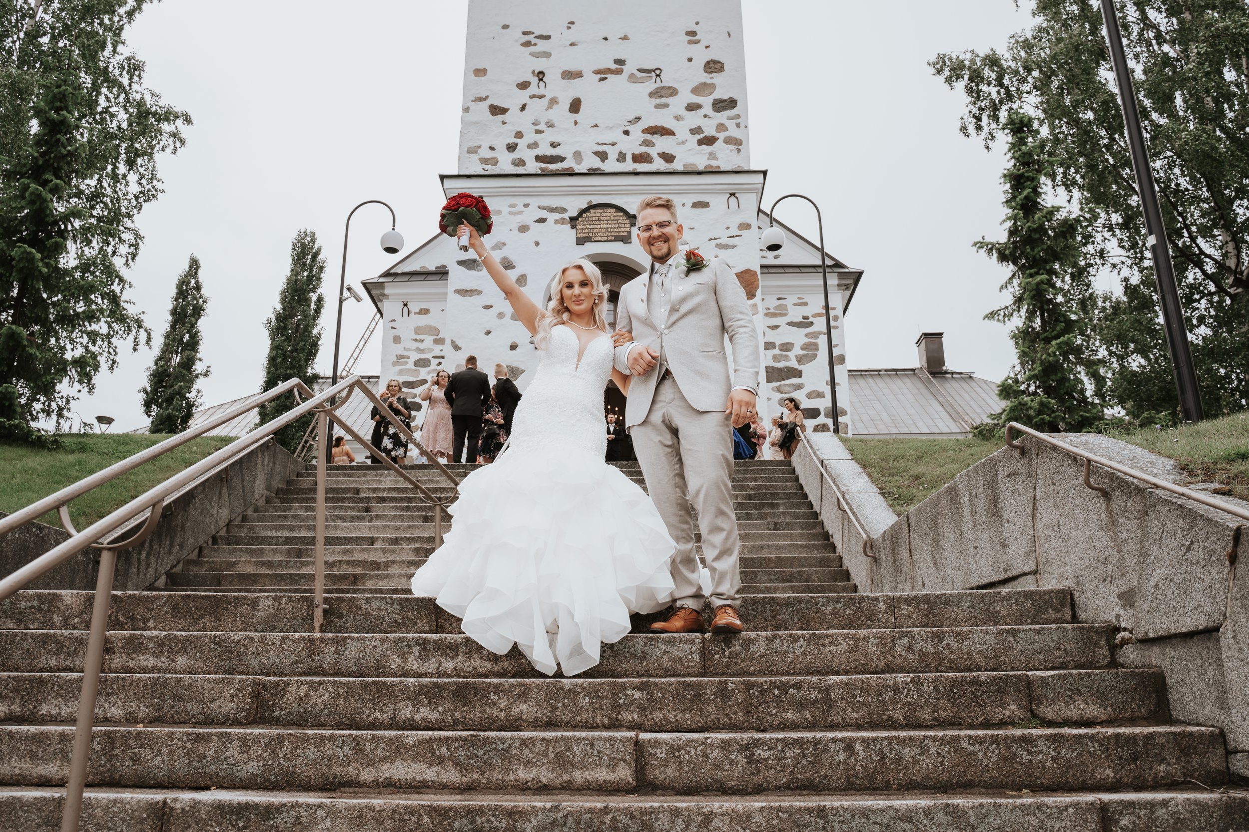 bride and groom on church steps, holding bouquet, celebrating wedding