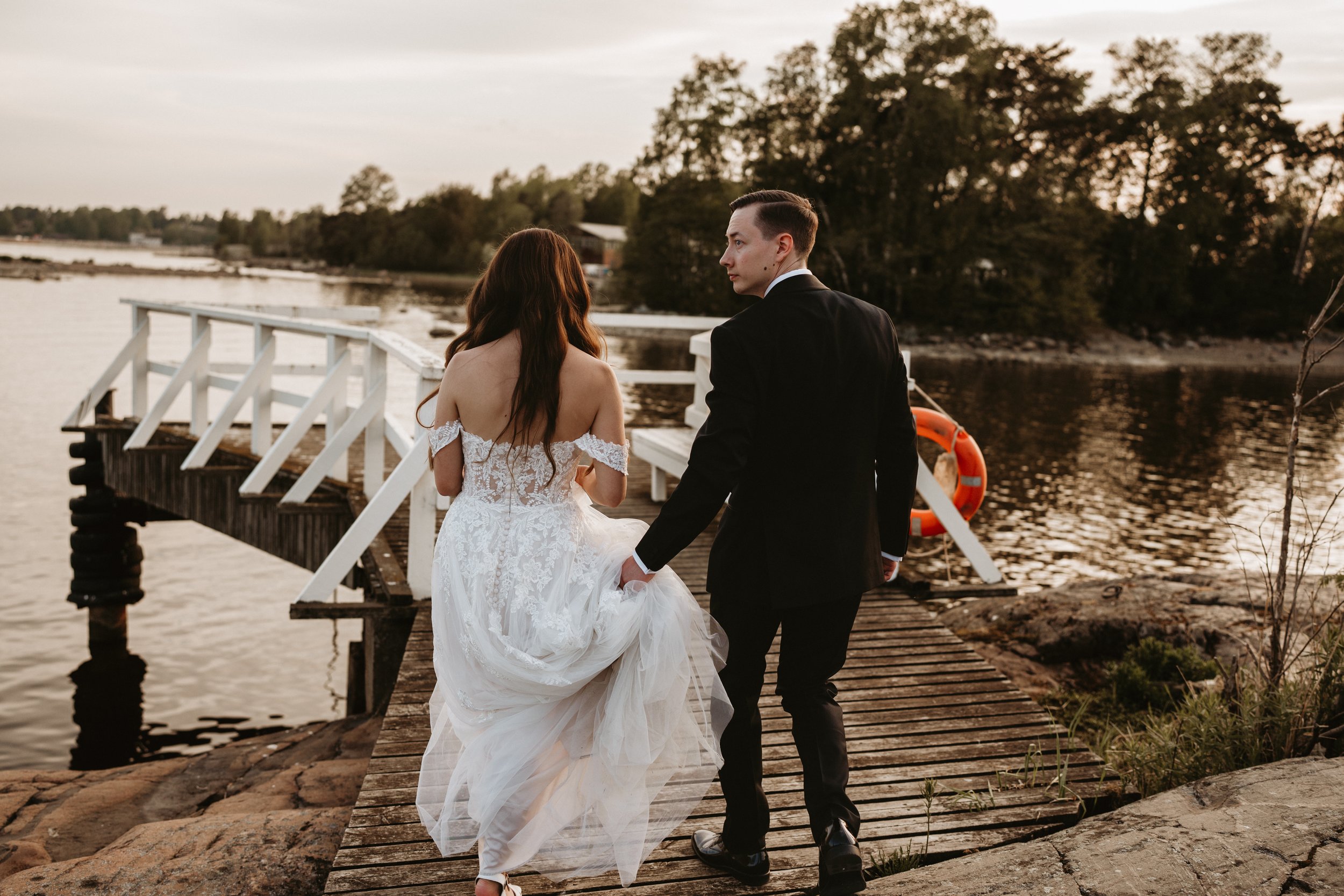 Bride and groom walking on wooden pier by water