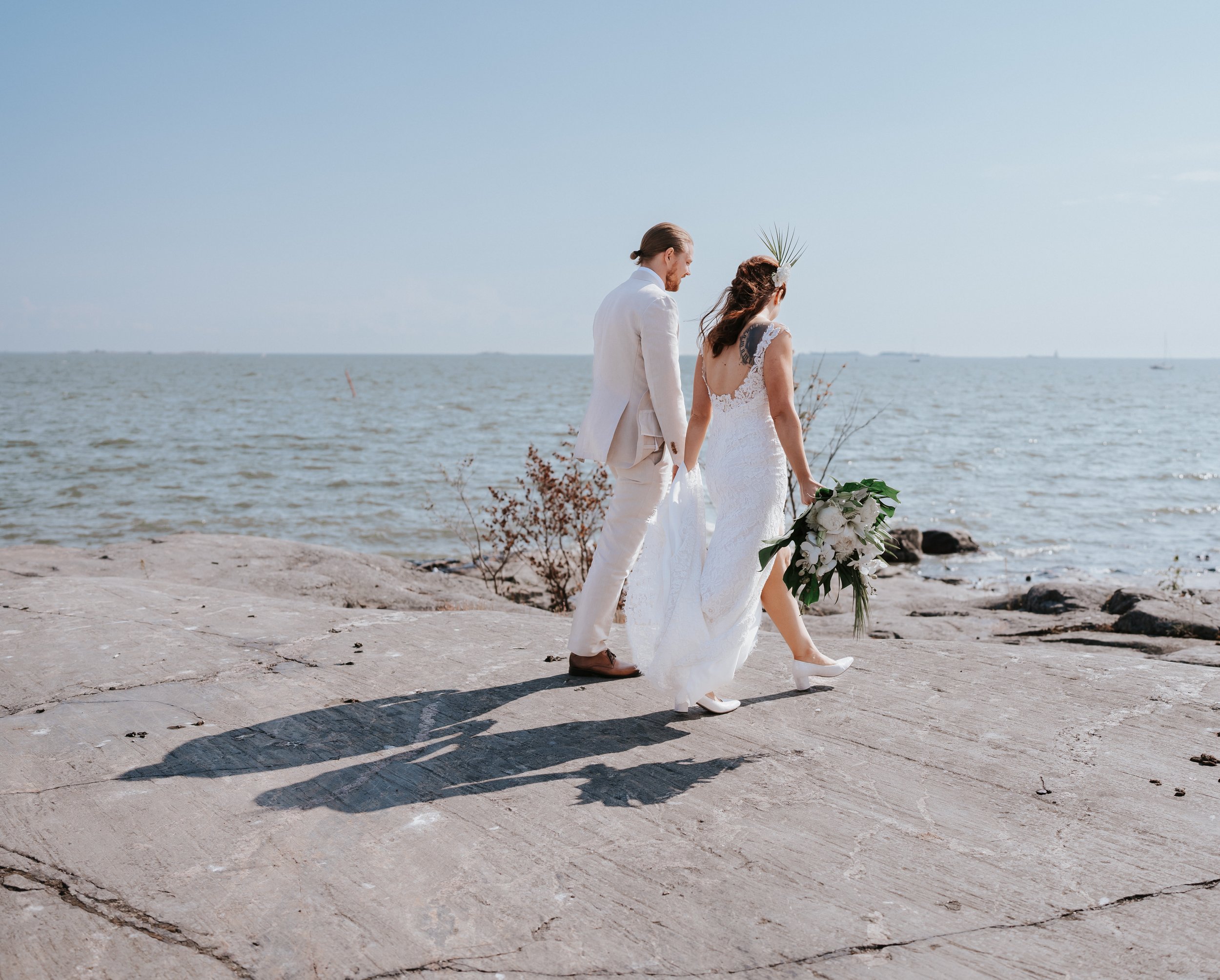 Bride and groom walking on rocky shore near ocean