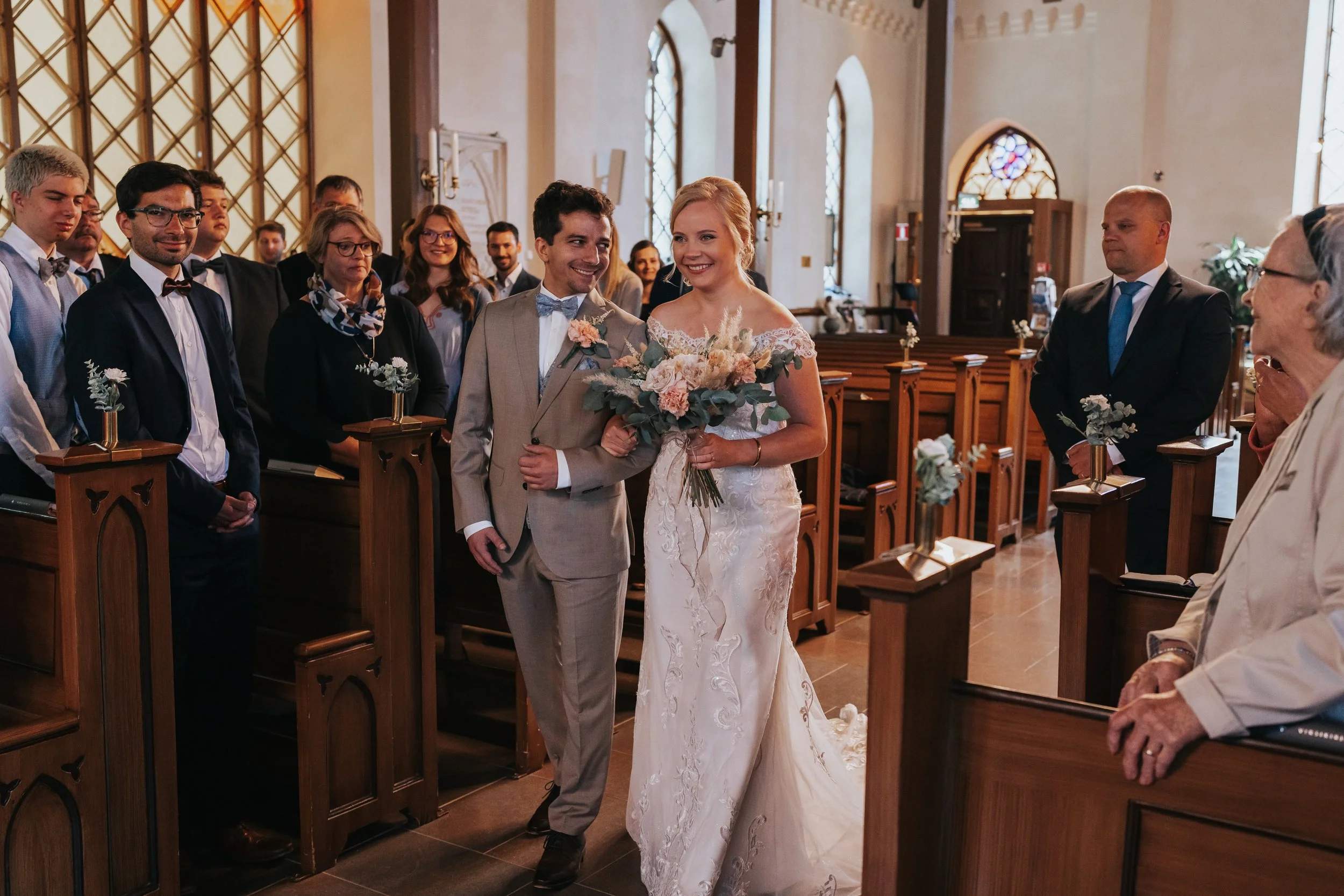 Bride and groom walking down the aisle in a church, surrounded by guests.