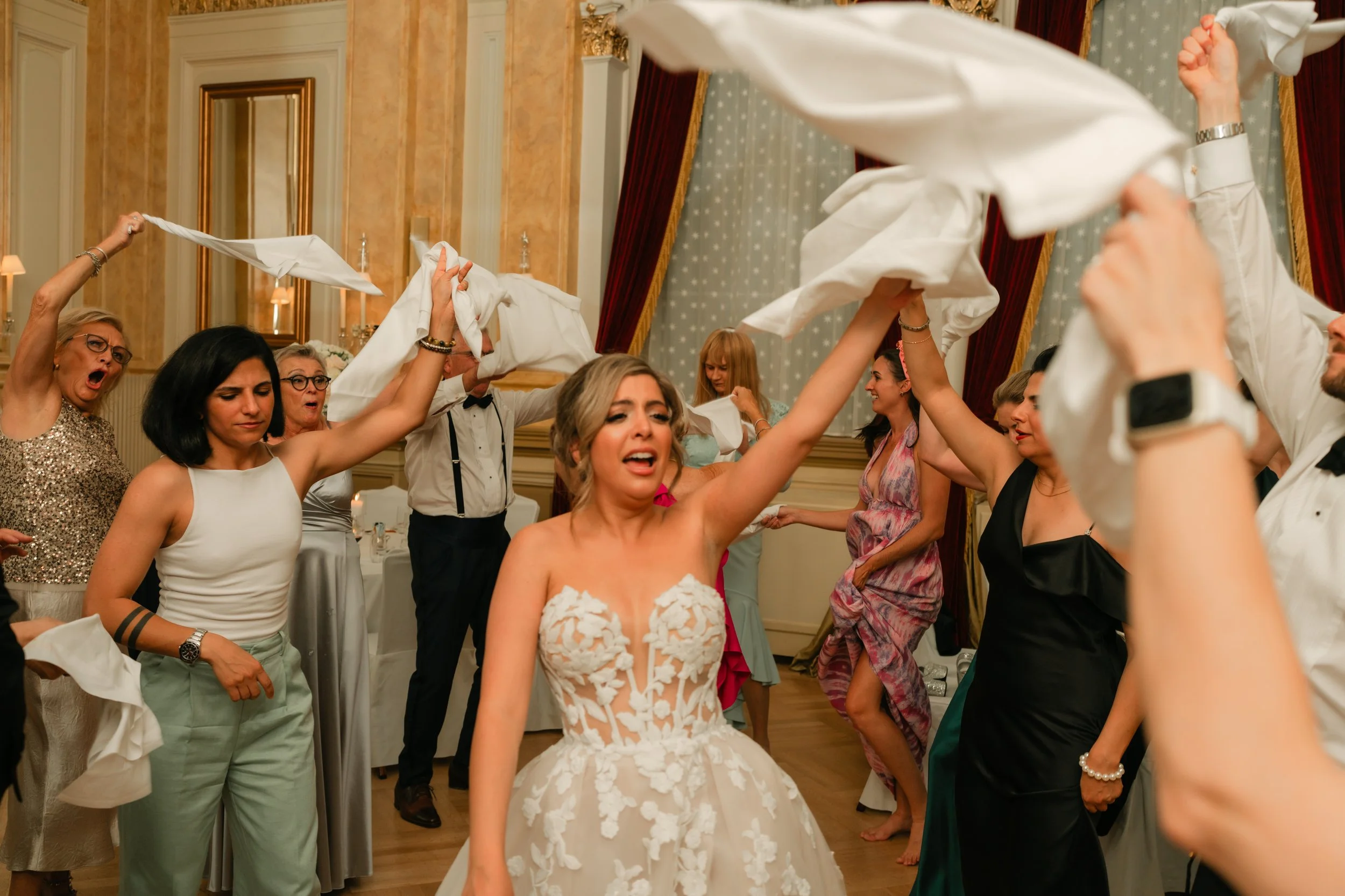 Wedding guests dancing, waving napkins, bride in white dress