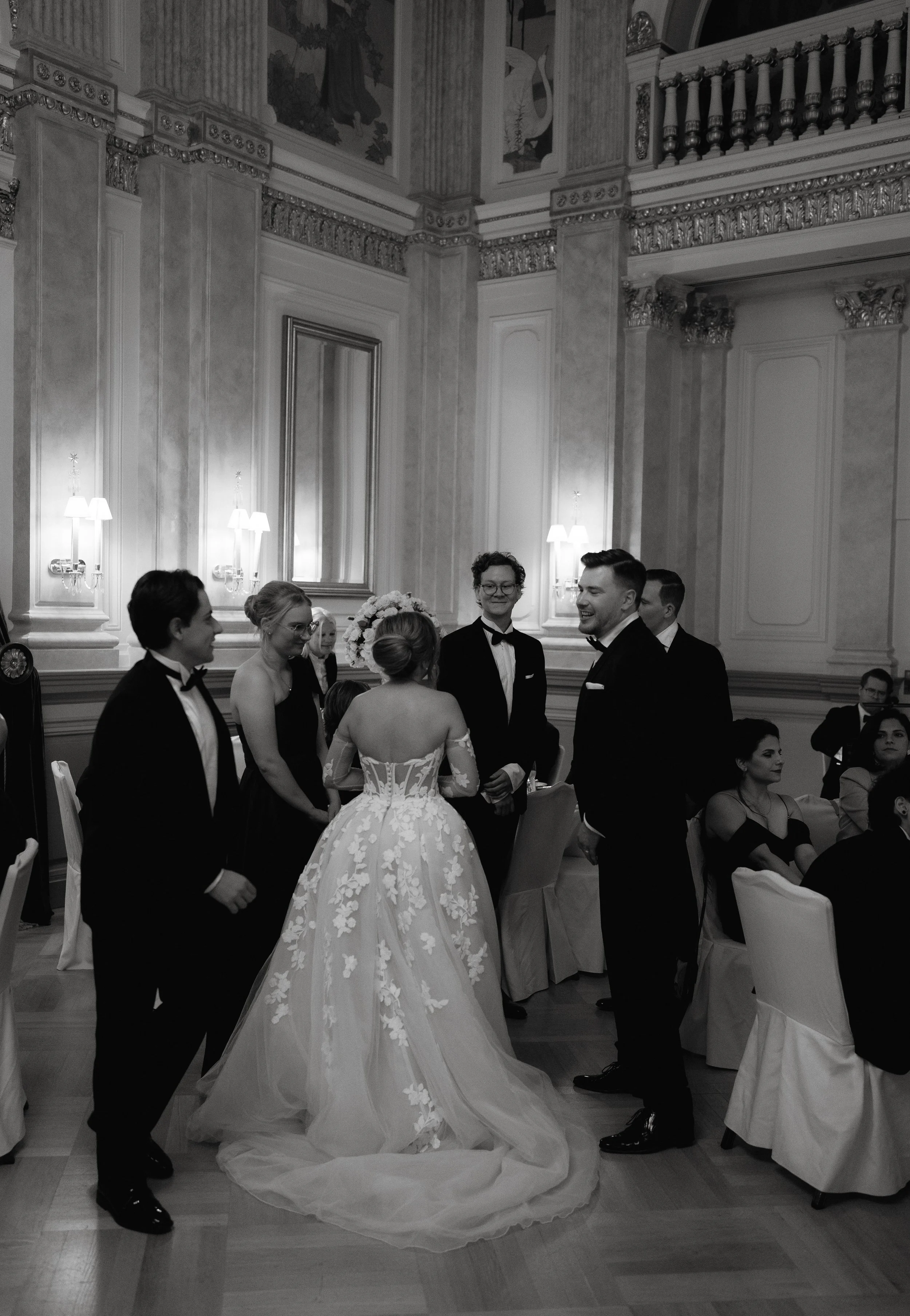 Elegant wedding reception, guests in formal attire, bride in gown with floral details, ornate ballroom setting