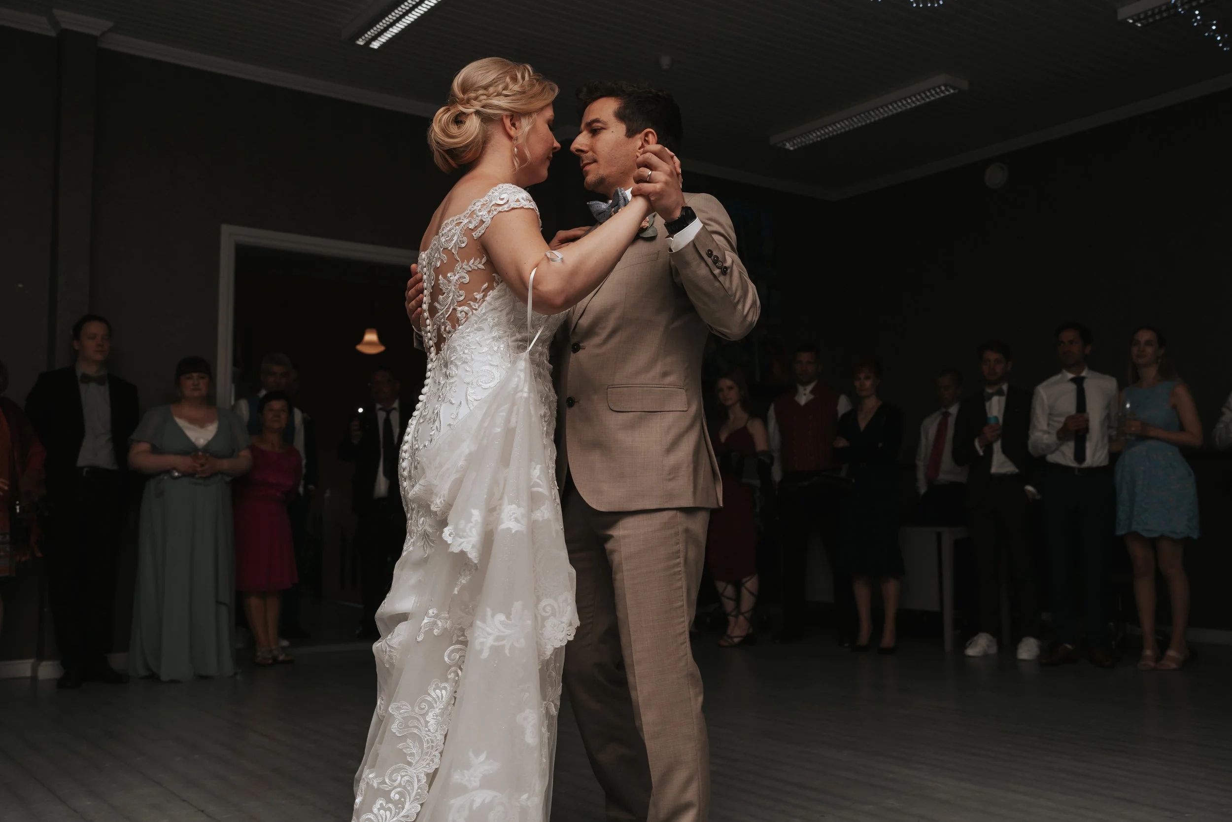 Bride and groom dancing at wedding reception with guests watching.