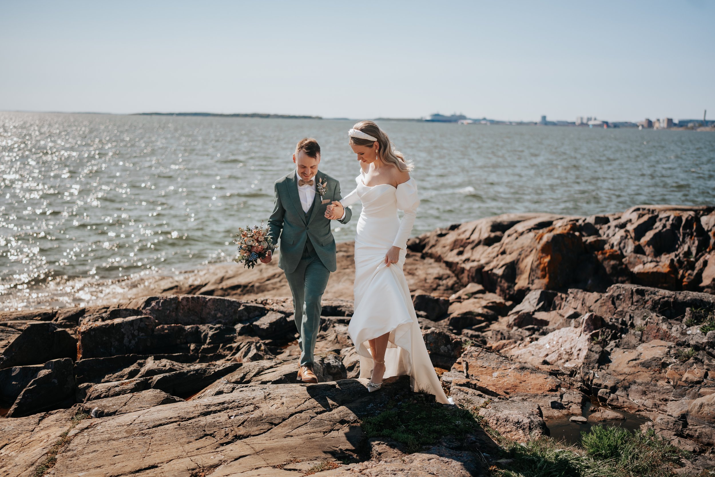 Wedding couple walking on rocky shore with ocean background