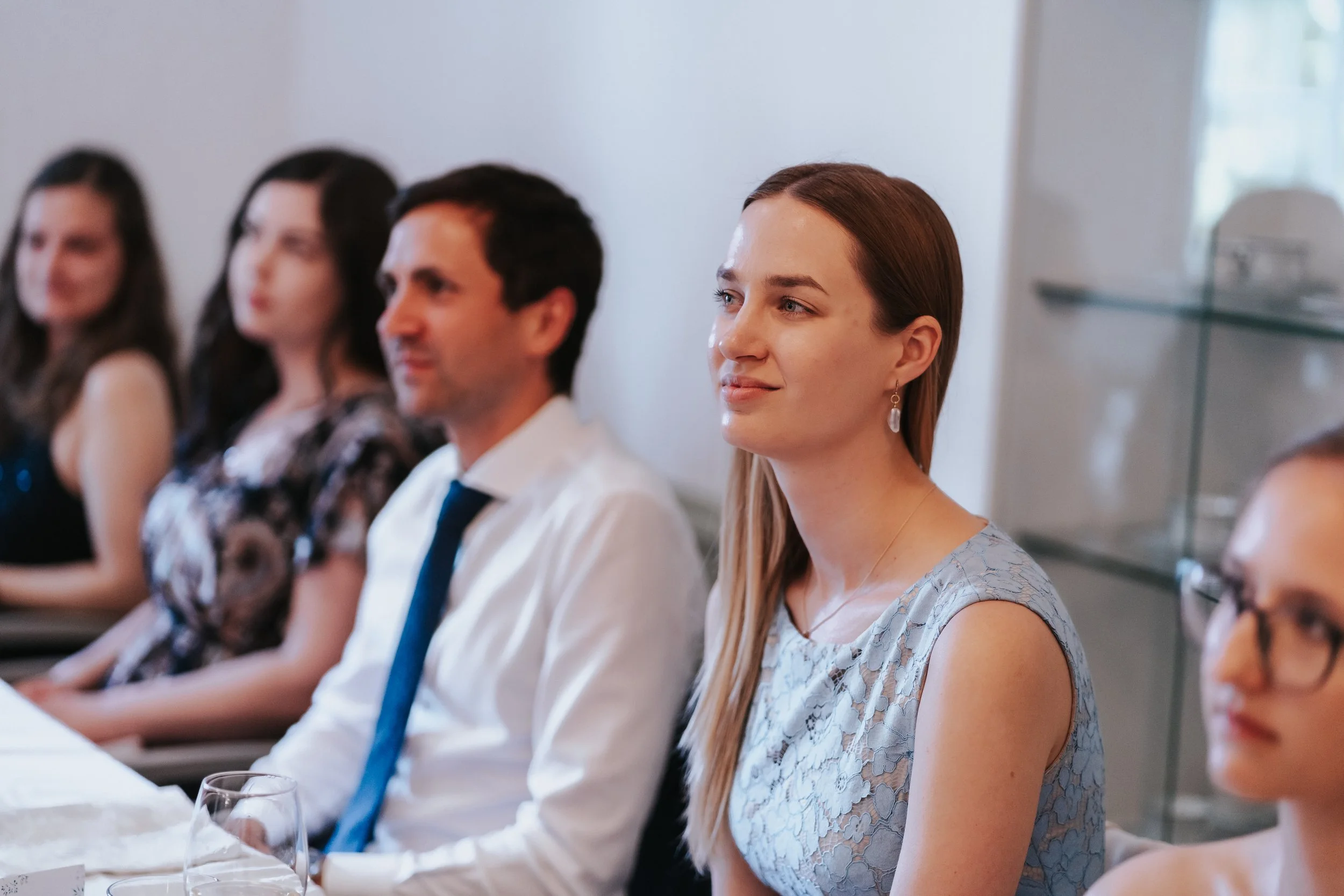 People sitting at a formal event, focused on a woman in a blue lace dress.