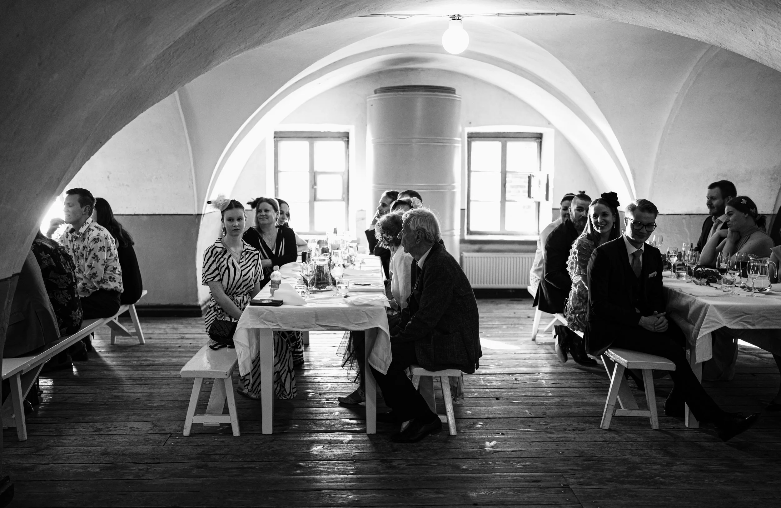 Black and white photo of a group of people seated at a long dining table in an arched-ceiling room.