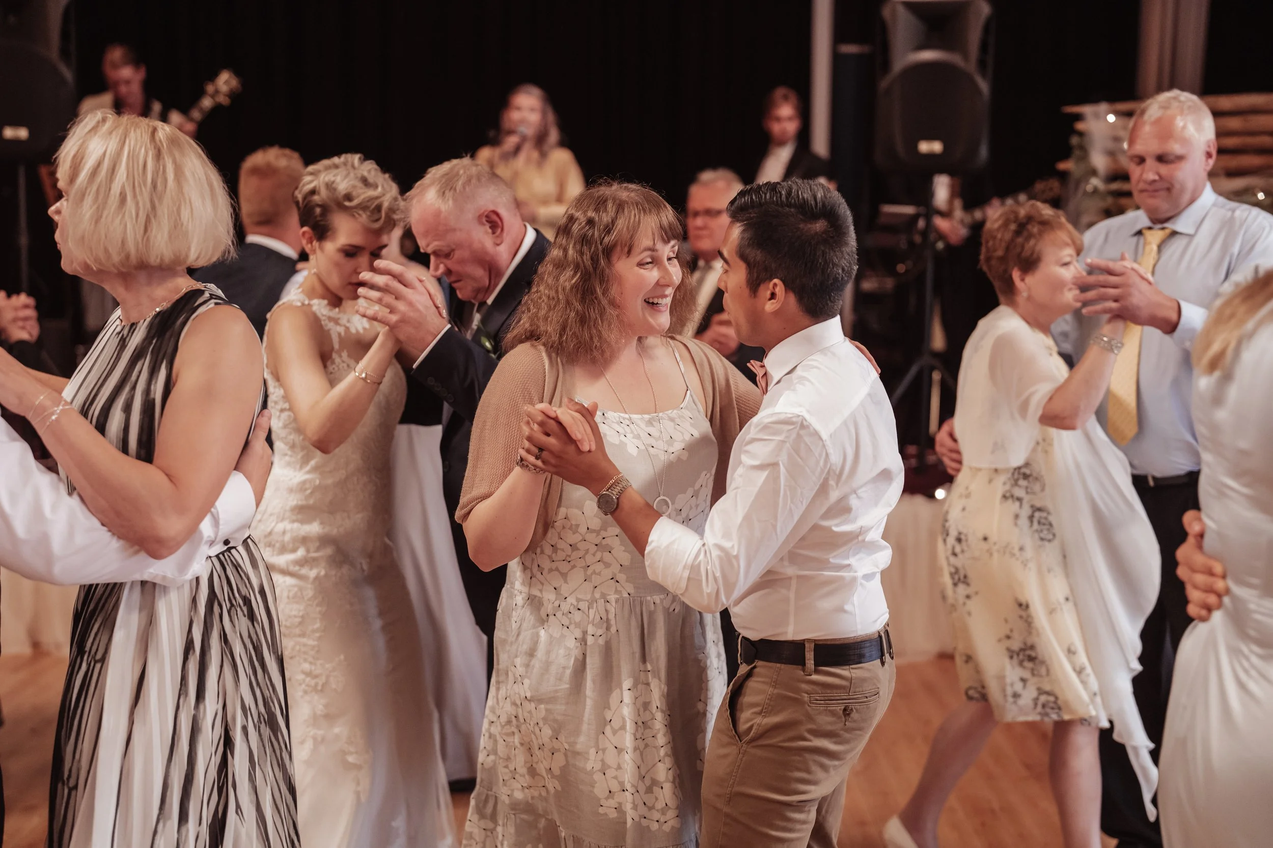 A group of people dancing at a wedding reception, dressed in formal attire, with a band performing in the background.