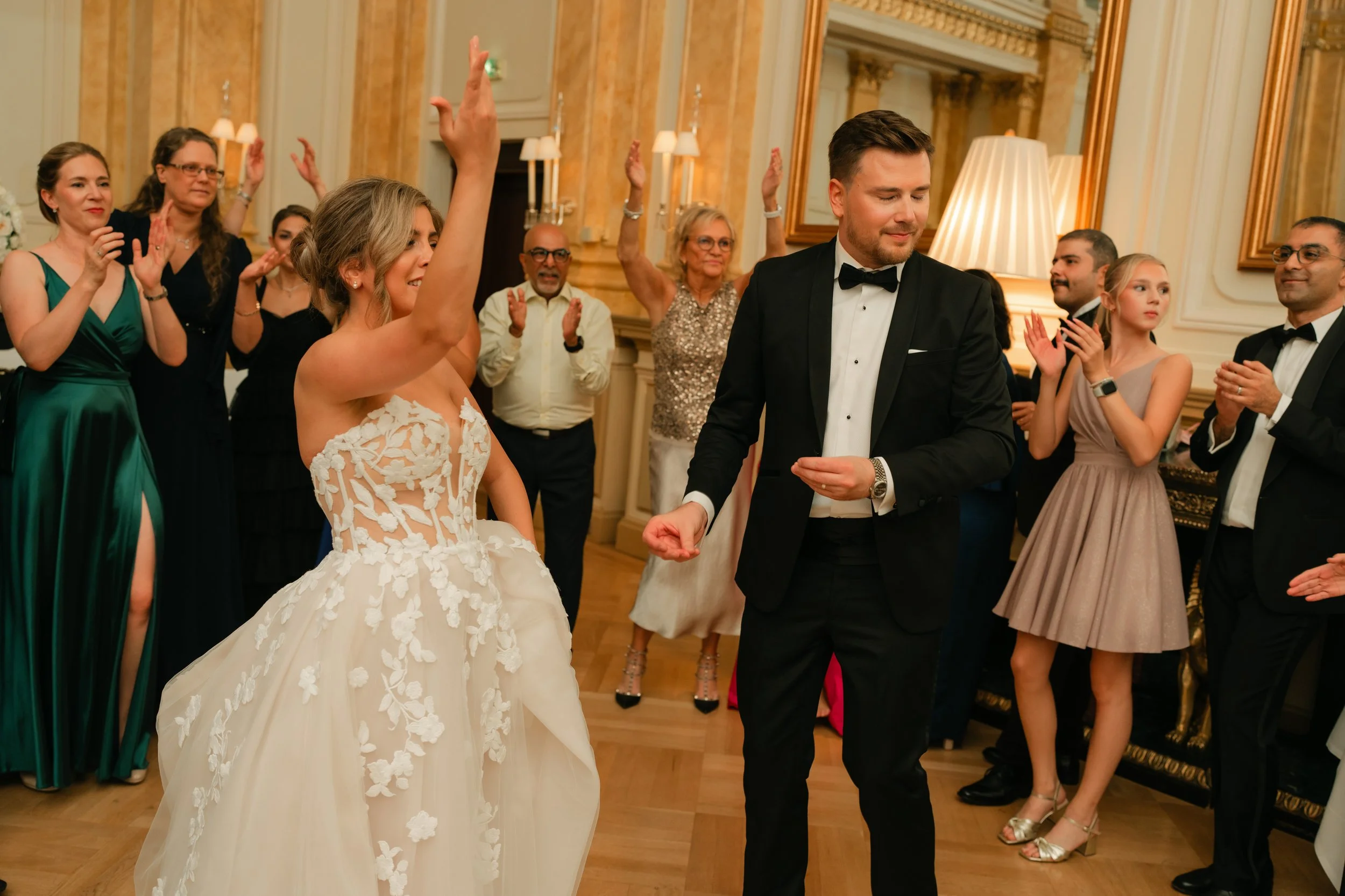 Bride and groom dancing at a wedding reception, surrounded by guests clapping, elegant setting.