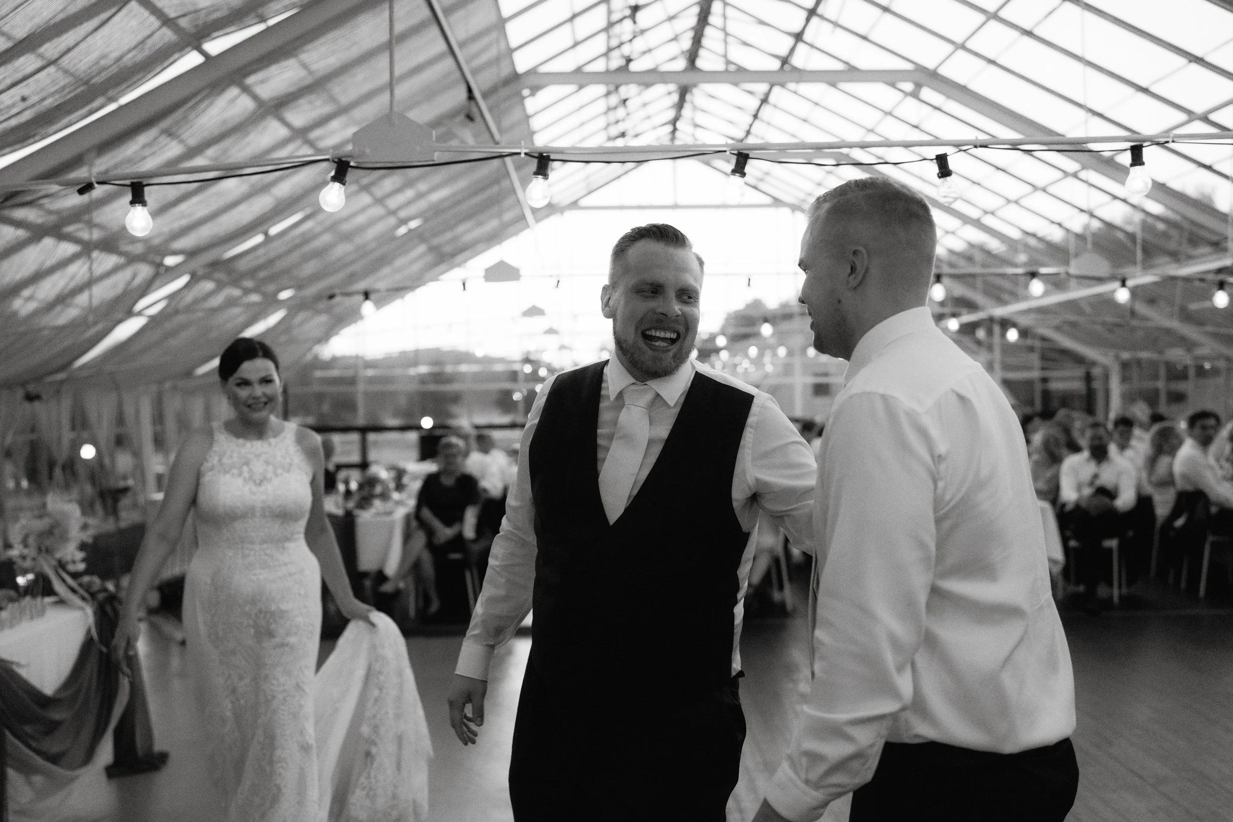 Wedding ceremony with bride in white dress and two men in formal attire smiling in a decorated indoor venue.