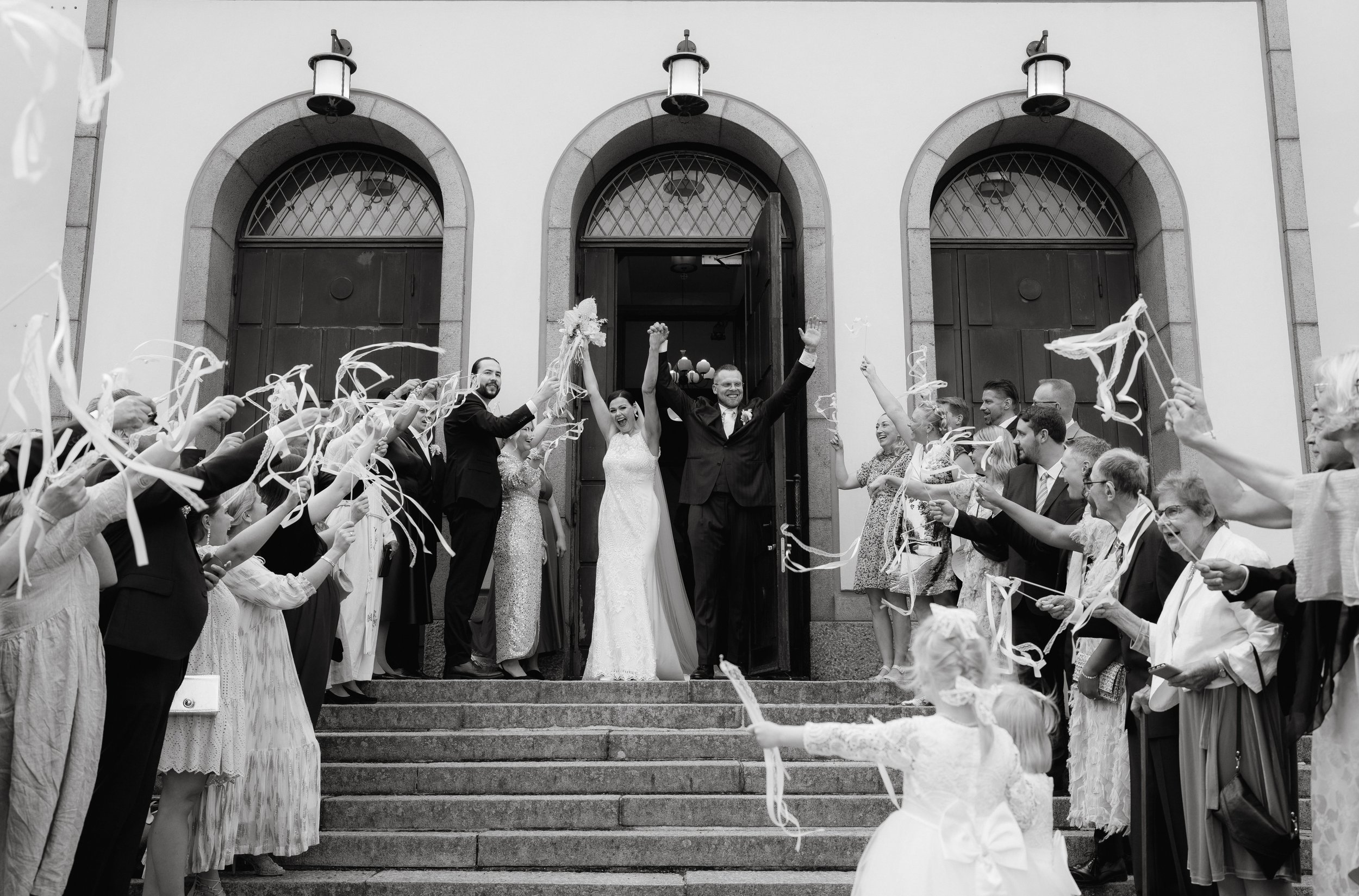 Black and white photo of newlyweds celebrating with guests outside a church.