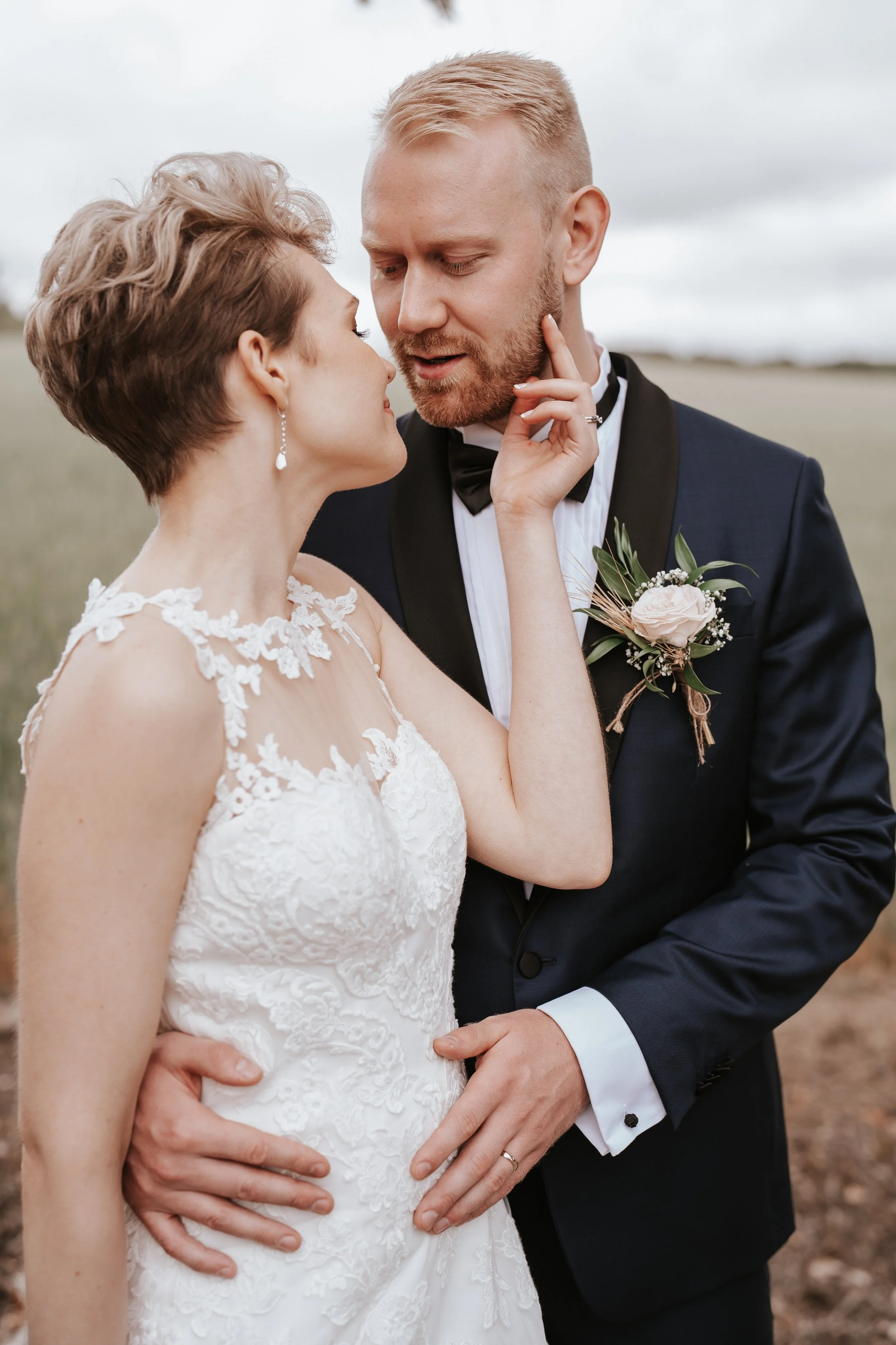 Bride and groom in elegant wedding attire, outdoors, close-up embrace.