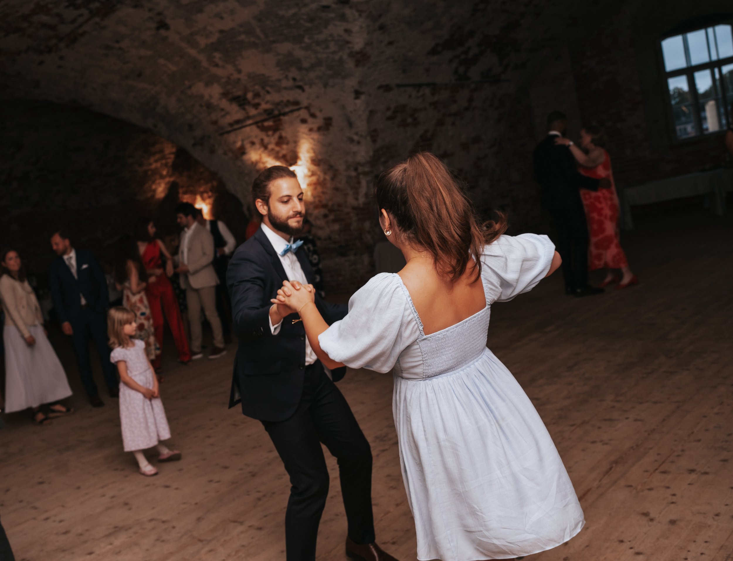 People dancing at a party in a dimly lit room with brick walls.