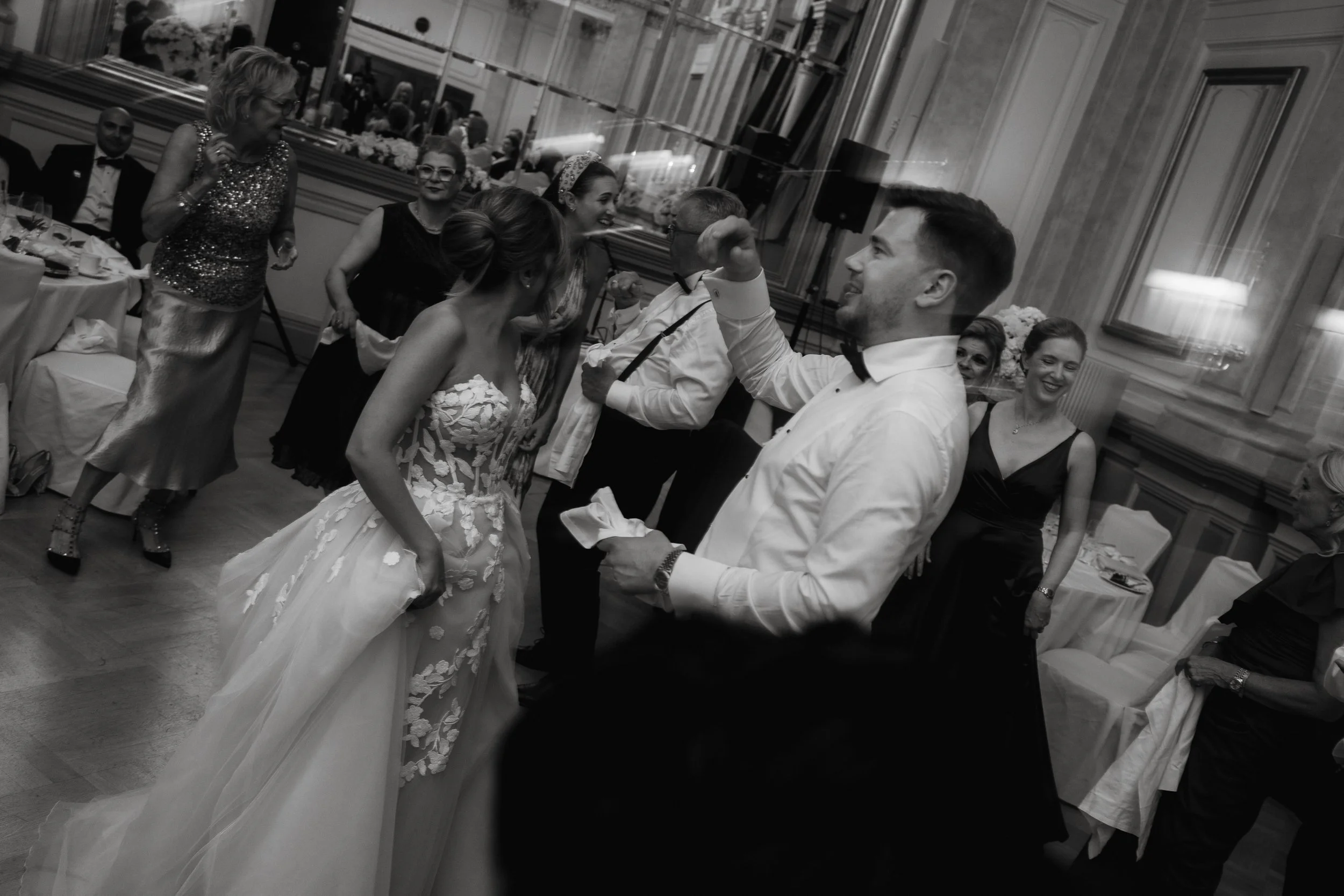 Wedding reception dance, bride and groom dancing, guests around, formal attire, elegant ballroom setting.