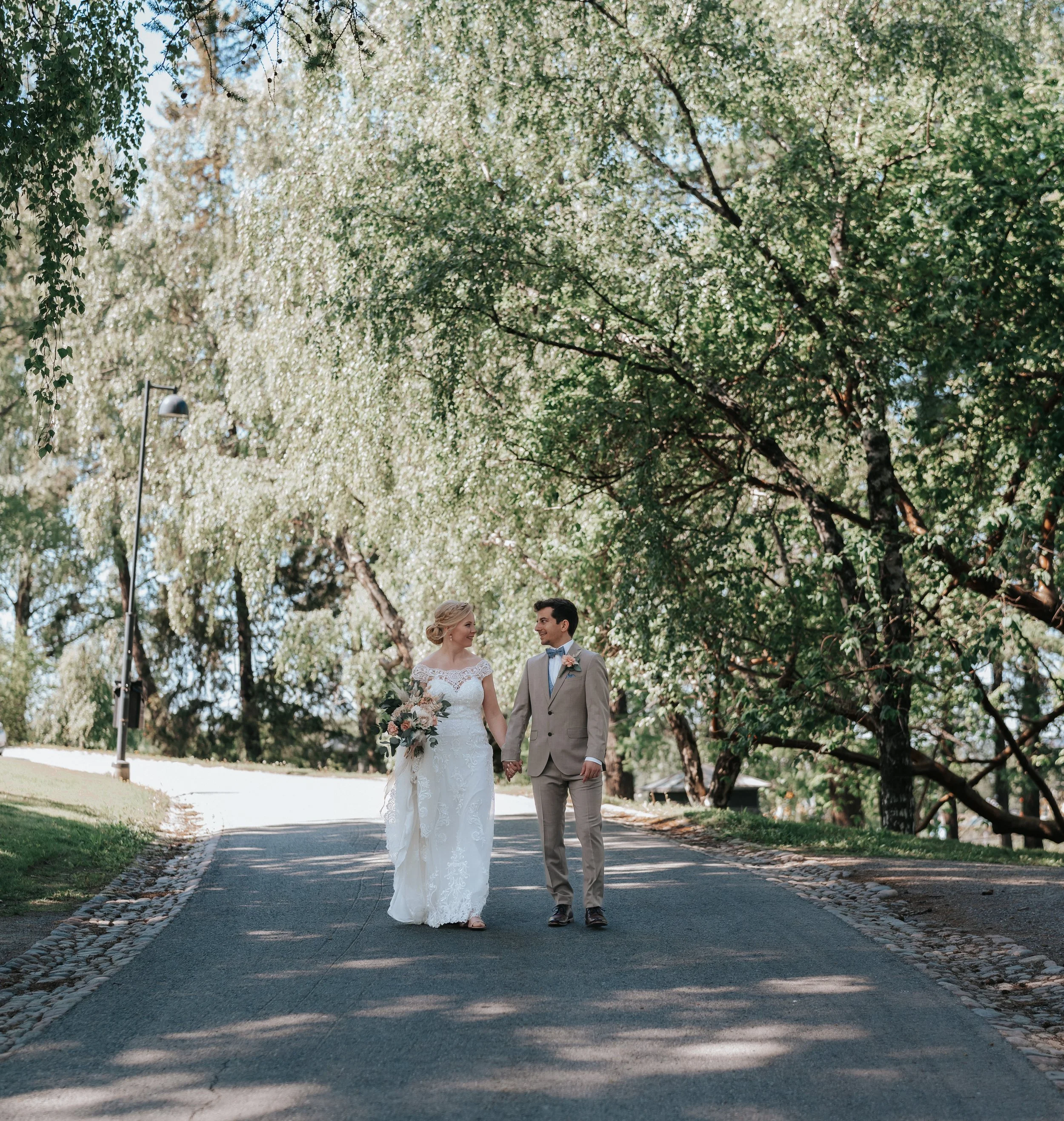 Bride and groom walking on a tree-lined path.