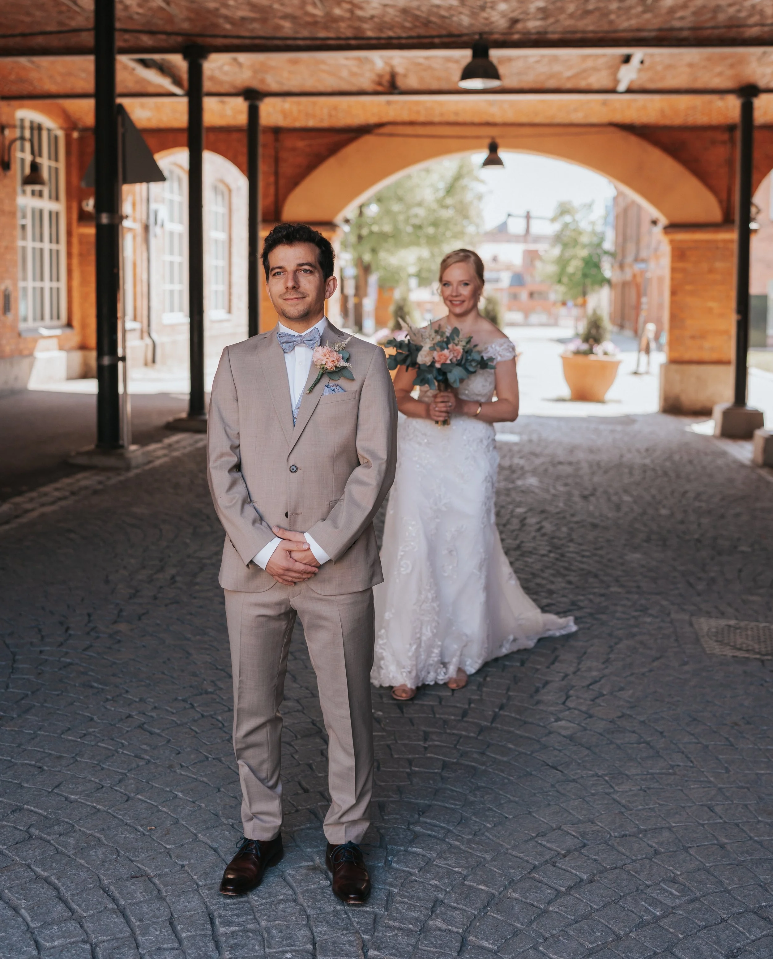 Bride and groom in formal attire under a brick archway.