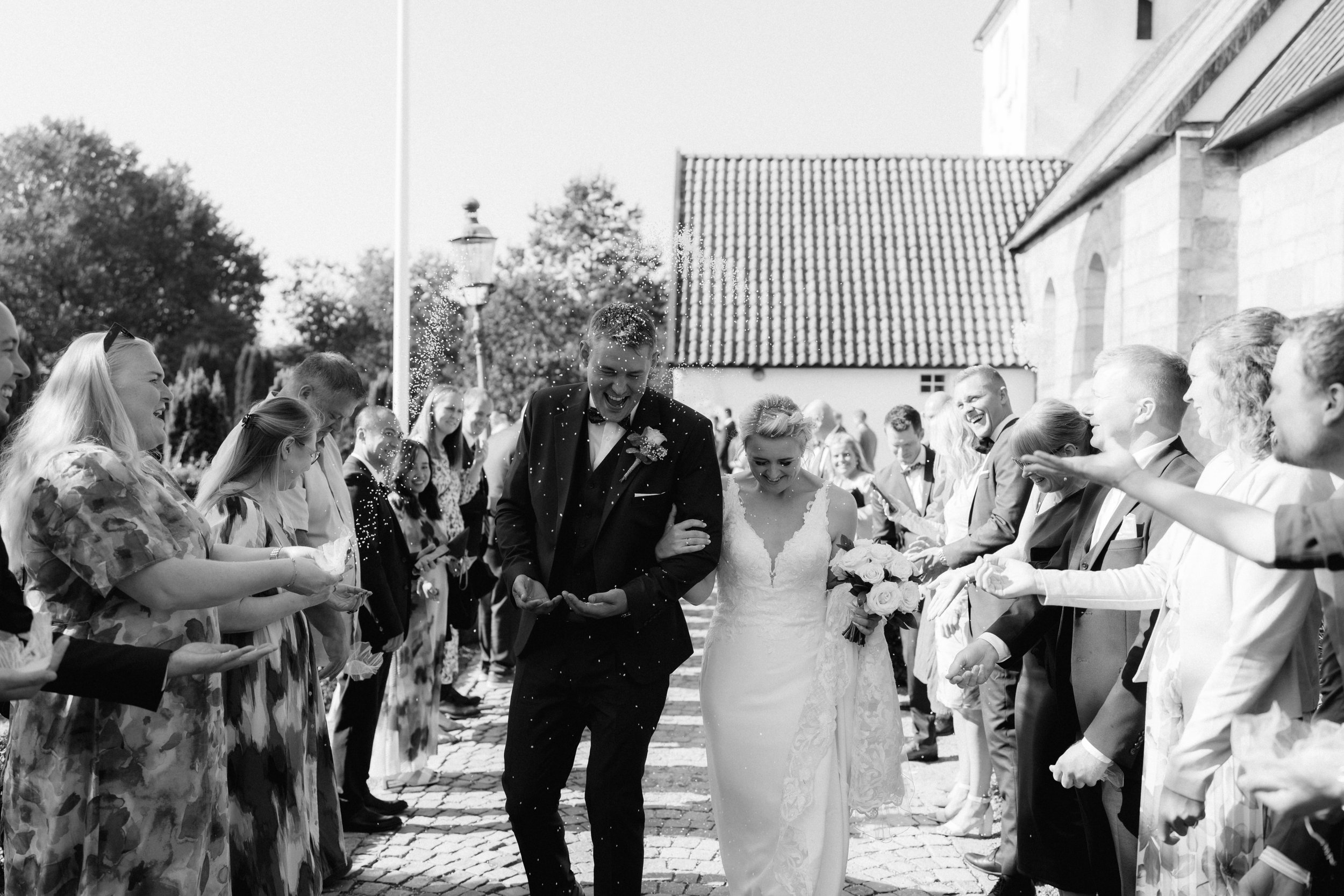 Newlywed couple walking through guests throwing confetti at an outdoor wedding ceremony.
