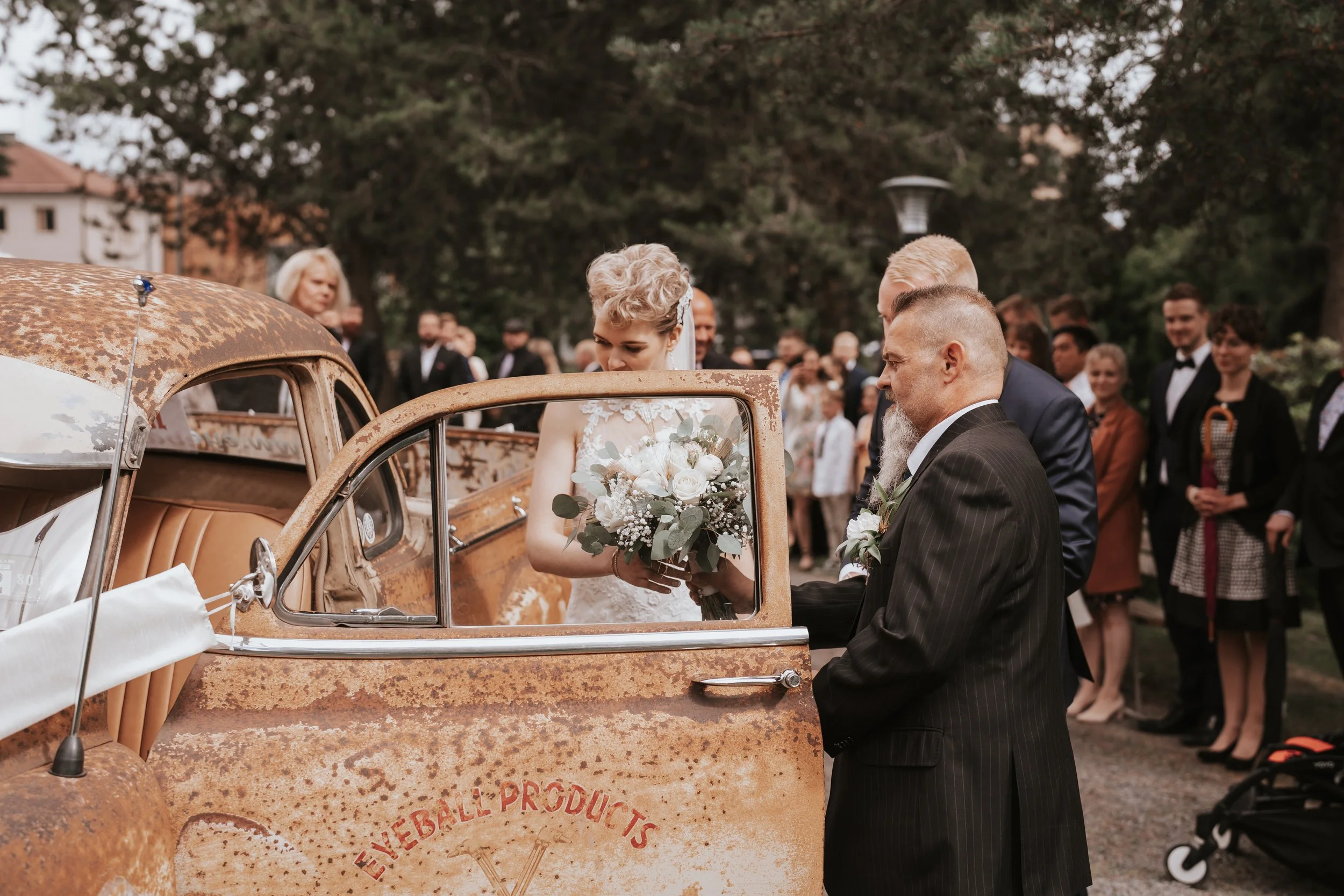 Bride holding bouquet near vintage car at outdoor wedding