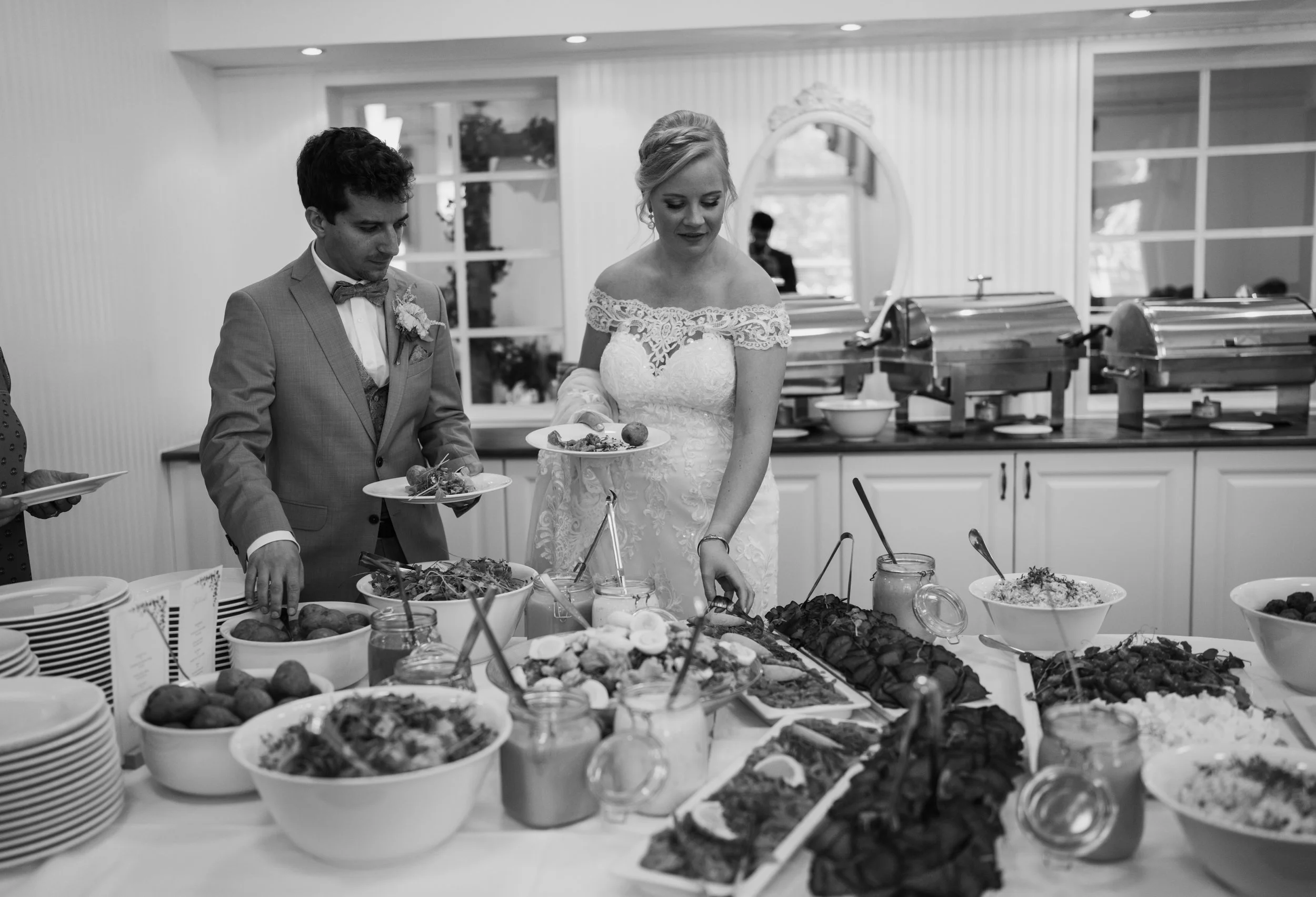 Bride and groom at a wedding buffet serving food on plates.
