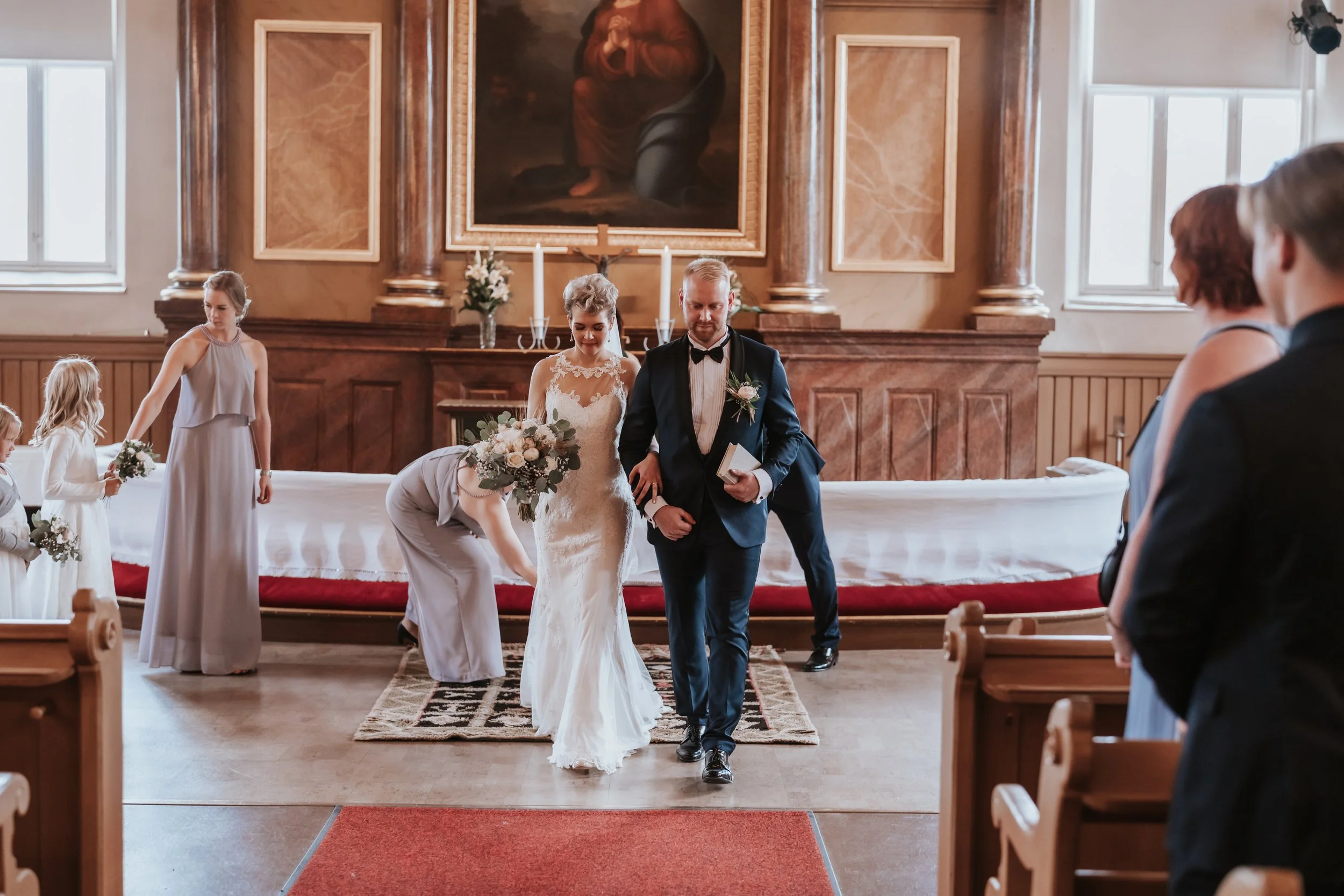 Bride and groom walking down the aisle in a church, with bridesmaids and flower girls holding bouquets.