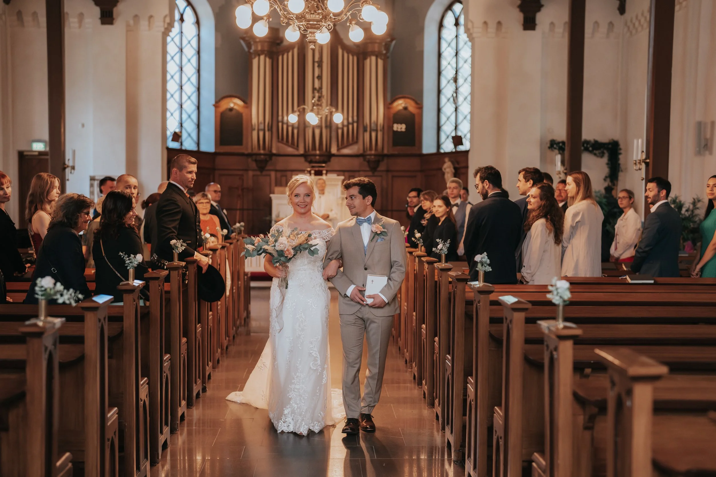 Bride and groom walking down the aisle in a church, surrounded by guests.