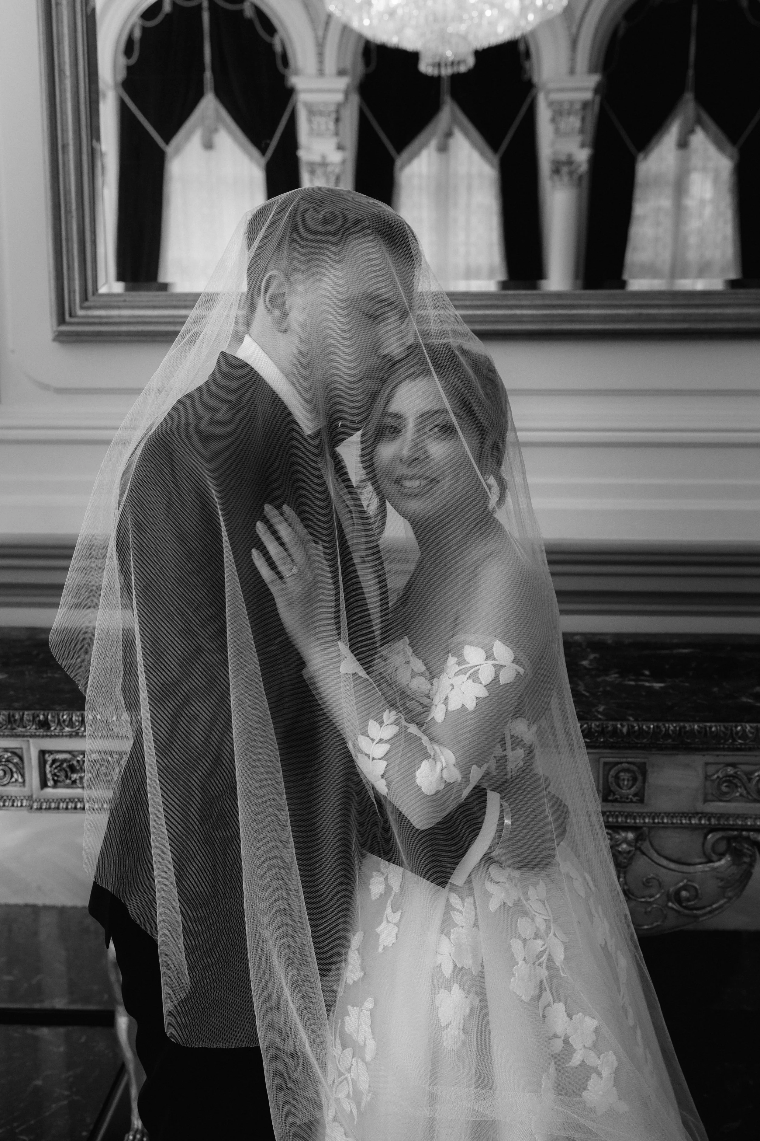 Black and white wedding photo of a couple embracing under a veil.