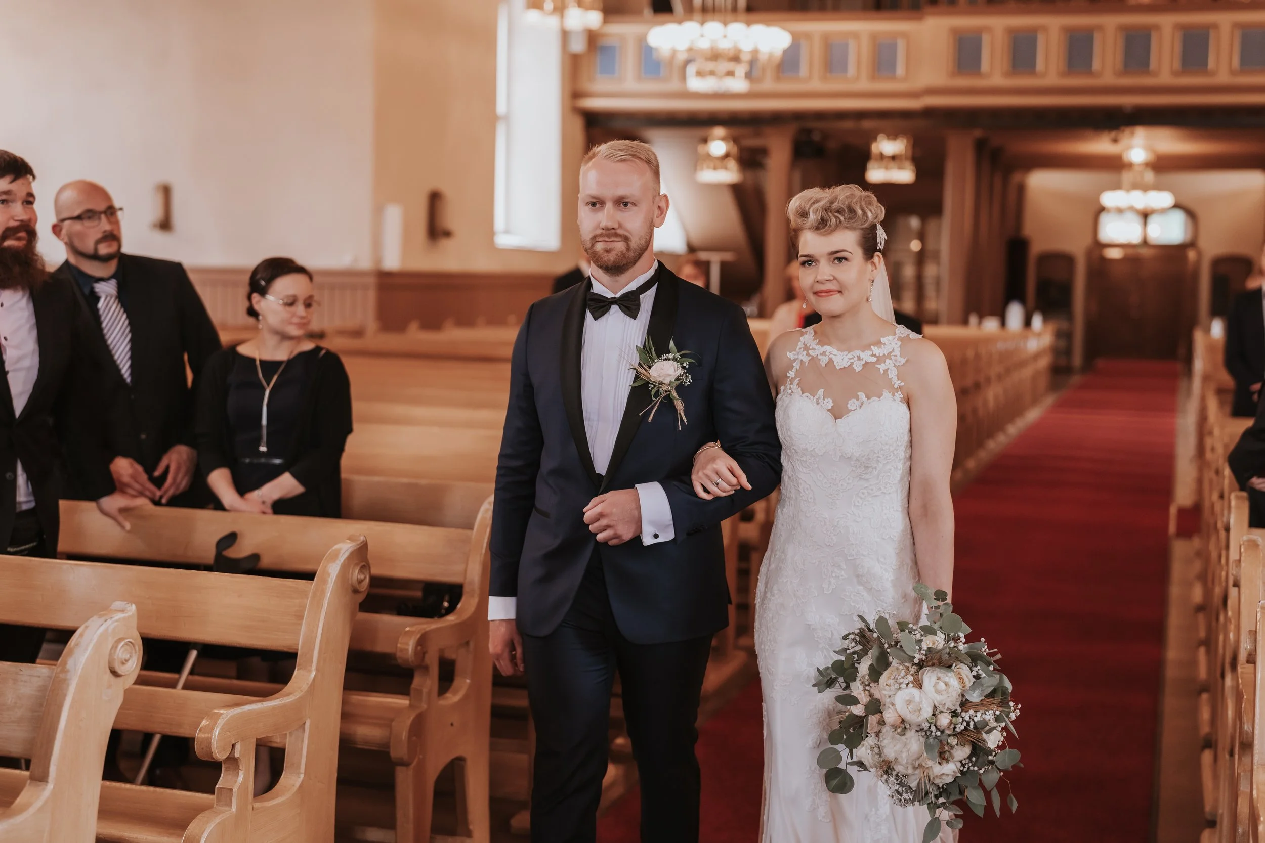 Bride and groom walking down church aisle, wedding ceremony, guests seated.