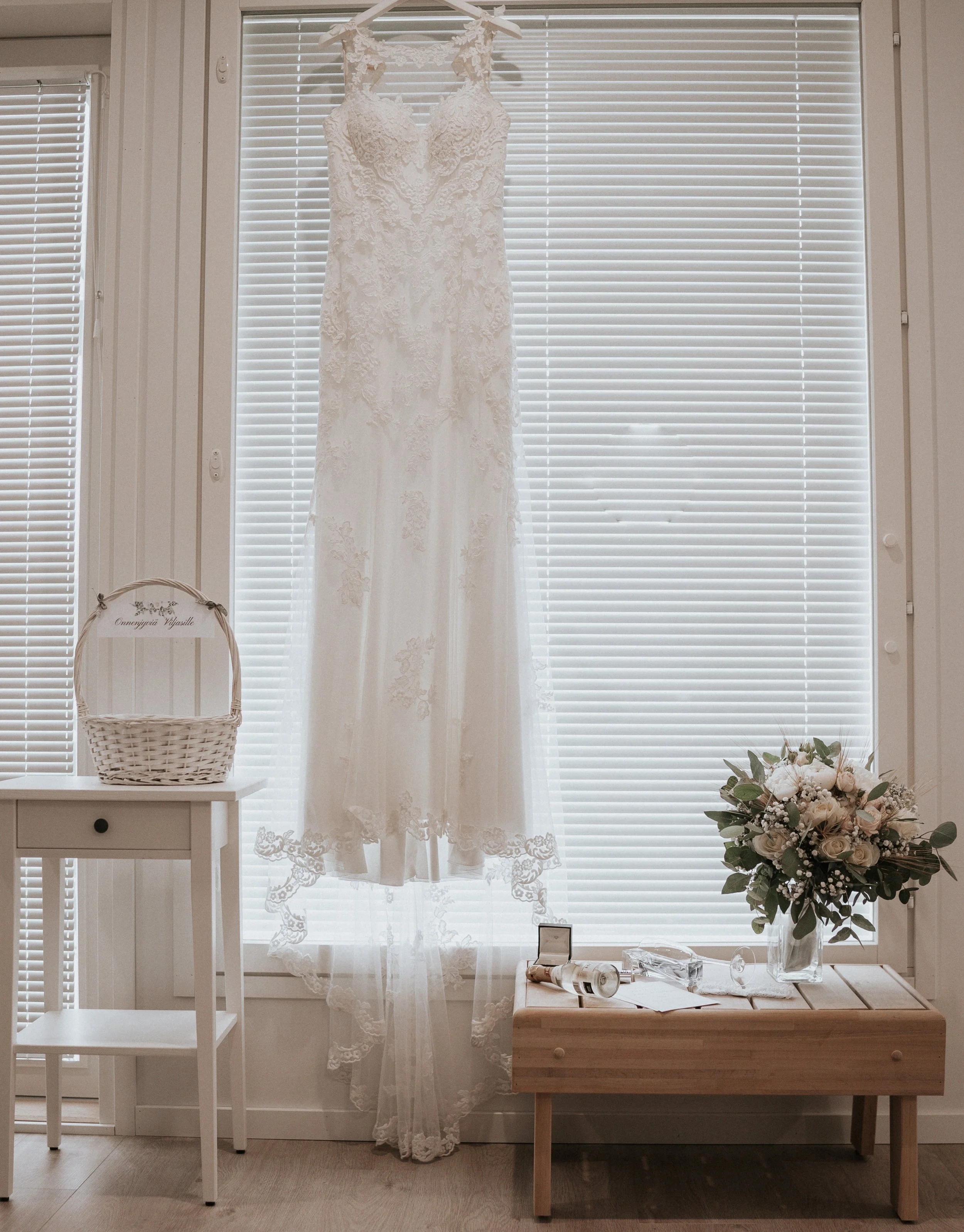 Wedding dress hanging beside a bouquet and bridal accessories.