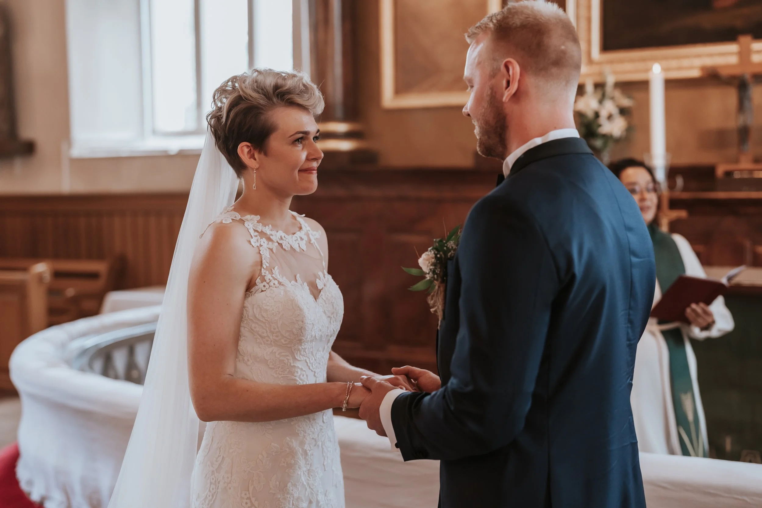 Wedding ceremony with couple exchanging vows in church, bride in white dress and groom in navy suit.