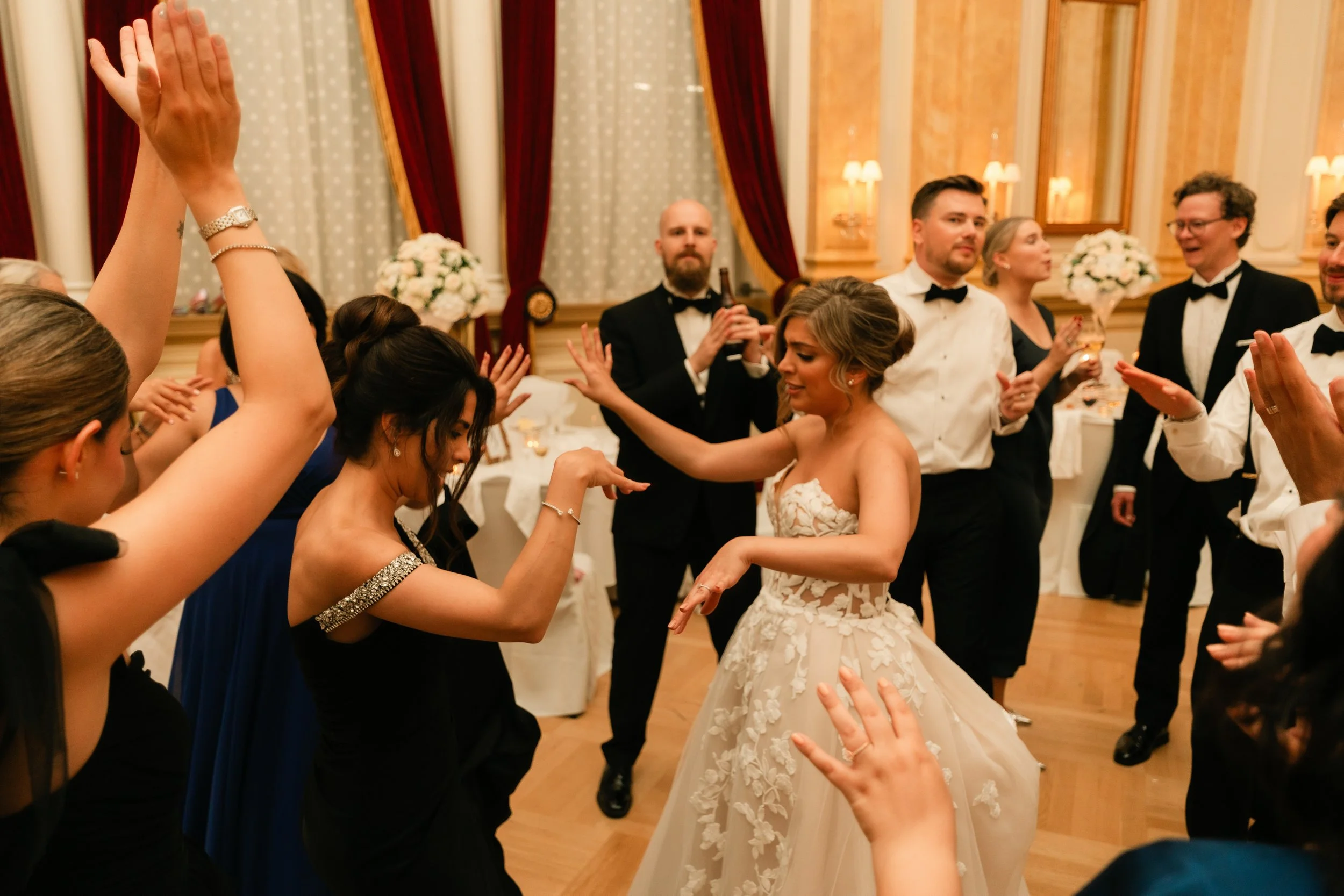 Wedding reception with guests dancing, bride in a white gown, ornate venue, joyful celebration.
