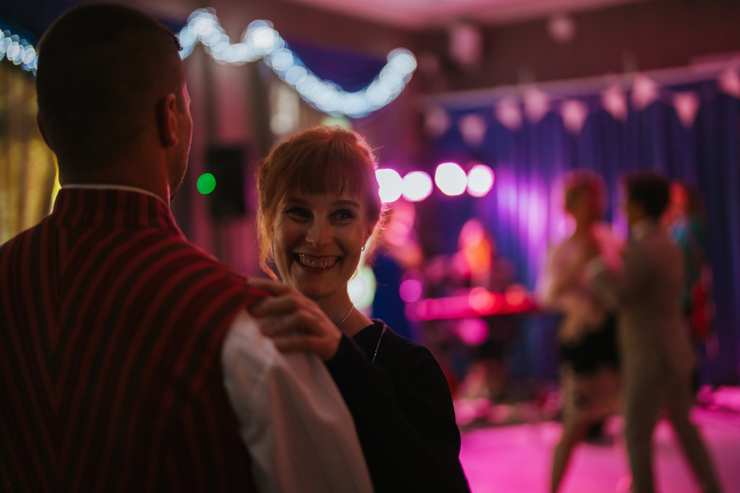 Couple dancing at a dimly lit party, with blurred background and colorful lights.