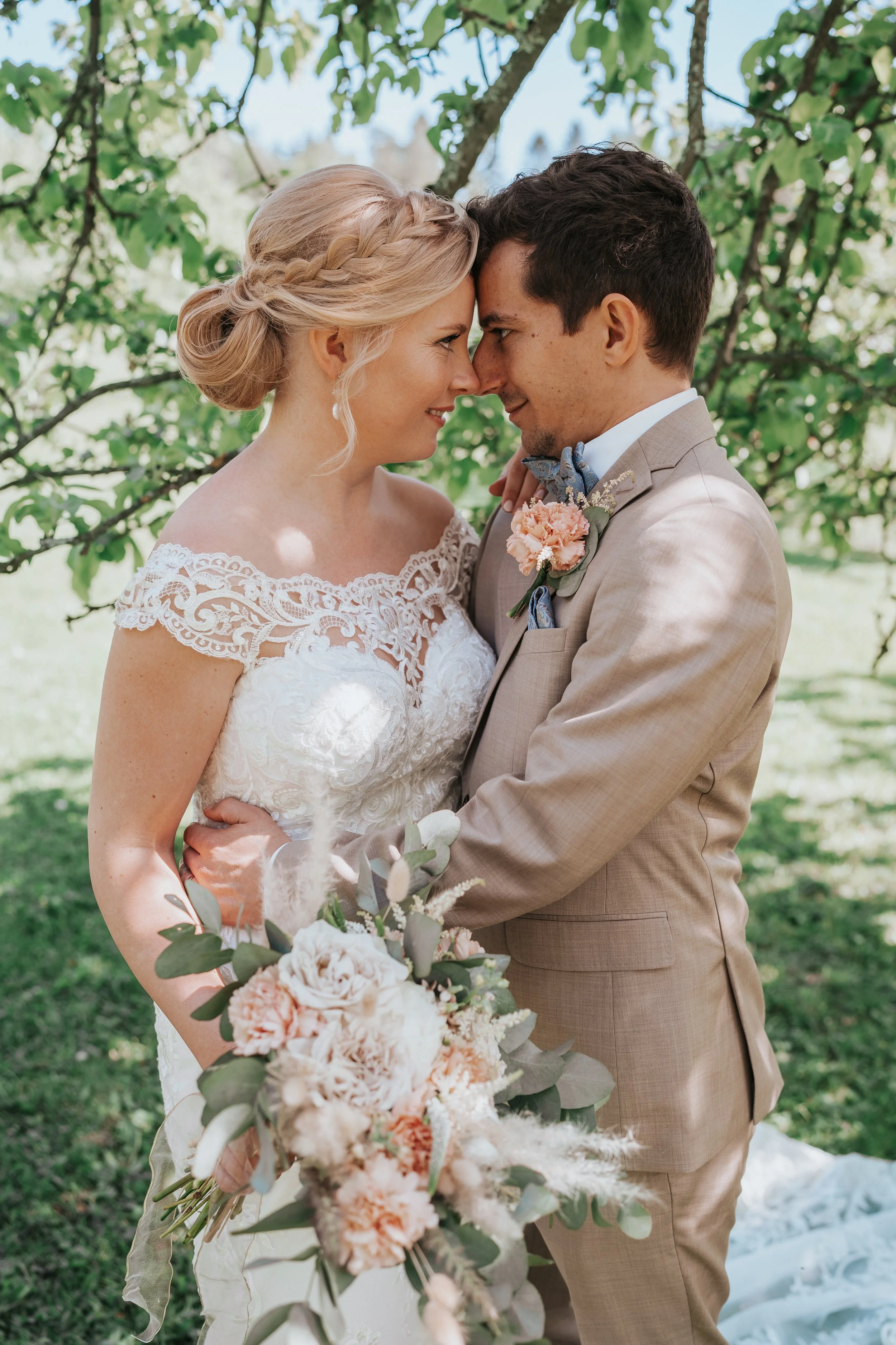 Bride and groom embrace under a tree during a wedding.