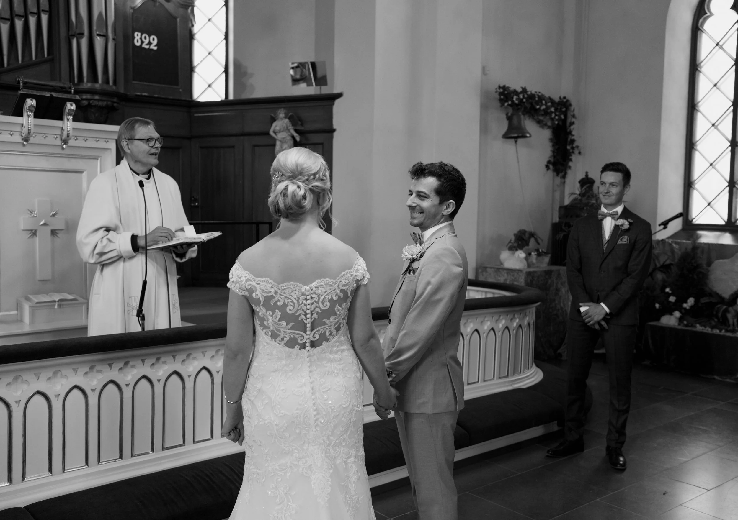 Bride and groom holding hands in church with officiant conducting ceremony.
