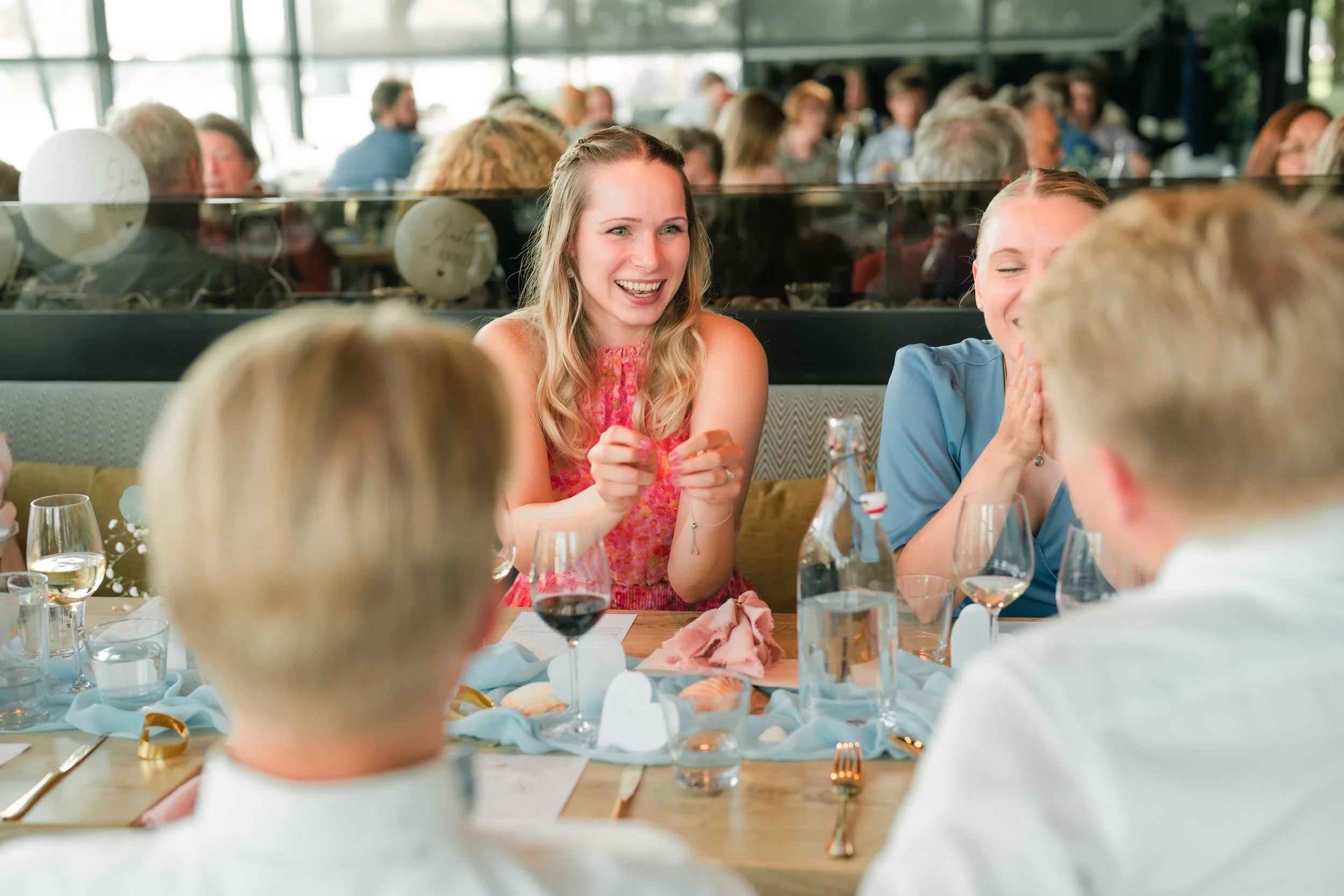 Group of people dining and laughing at a restaurant table with drinks and plates