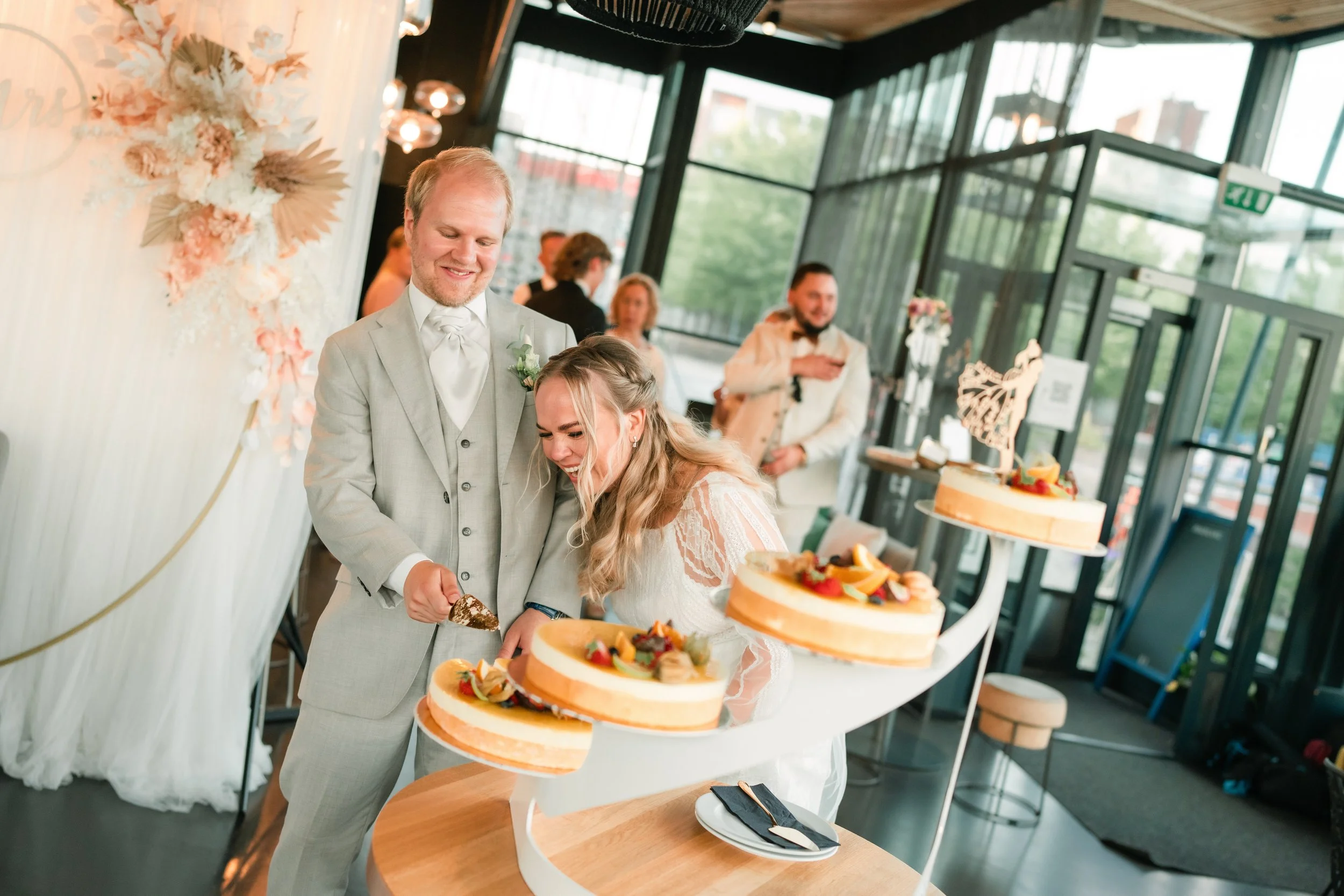 Bride and groom cutting a wedding cake with guests in the background.