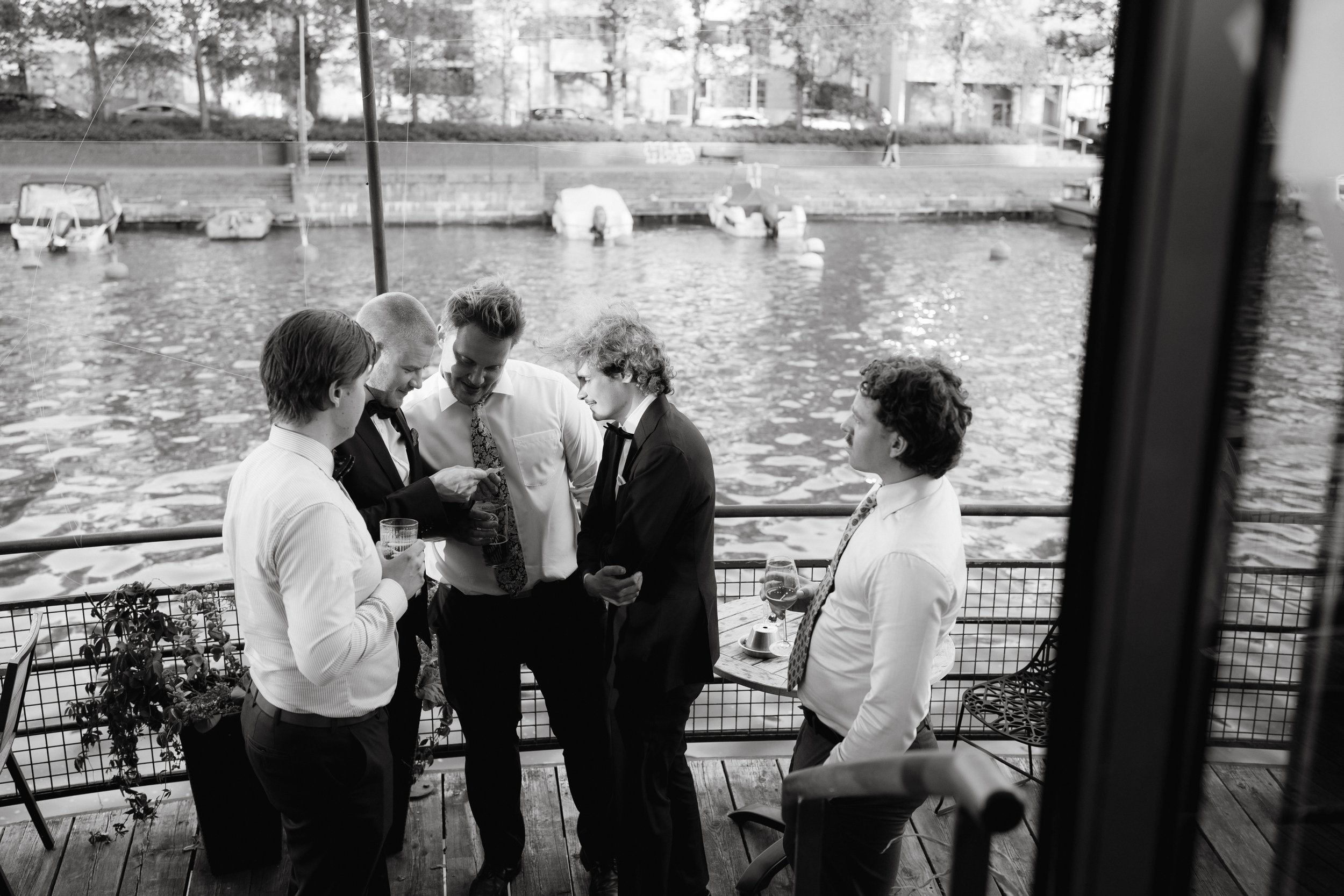 Five men in formal attire socializing by a riverside deck.