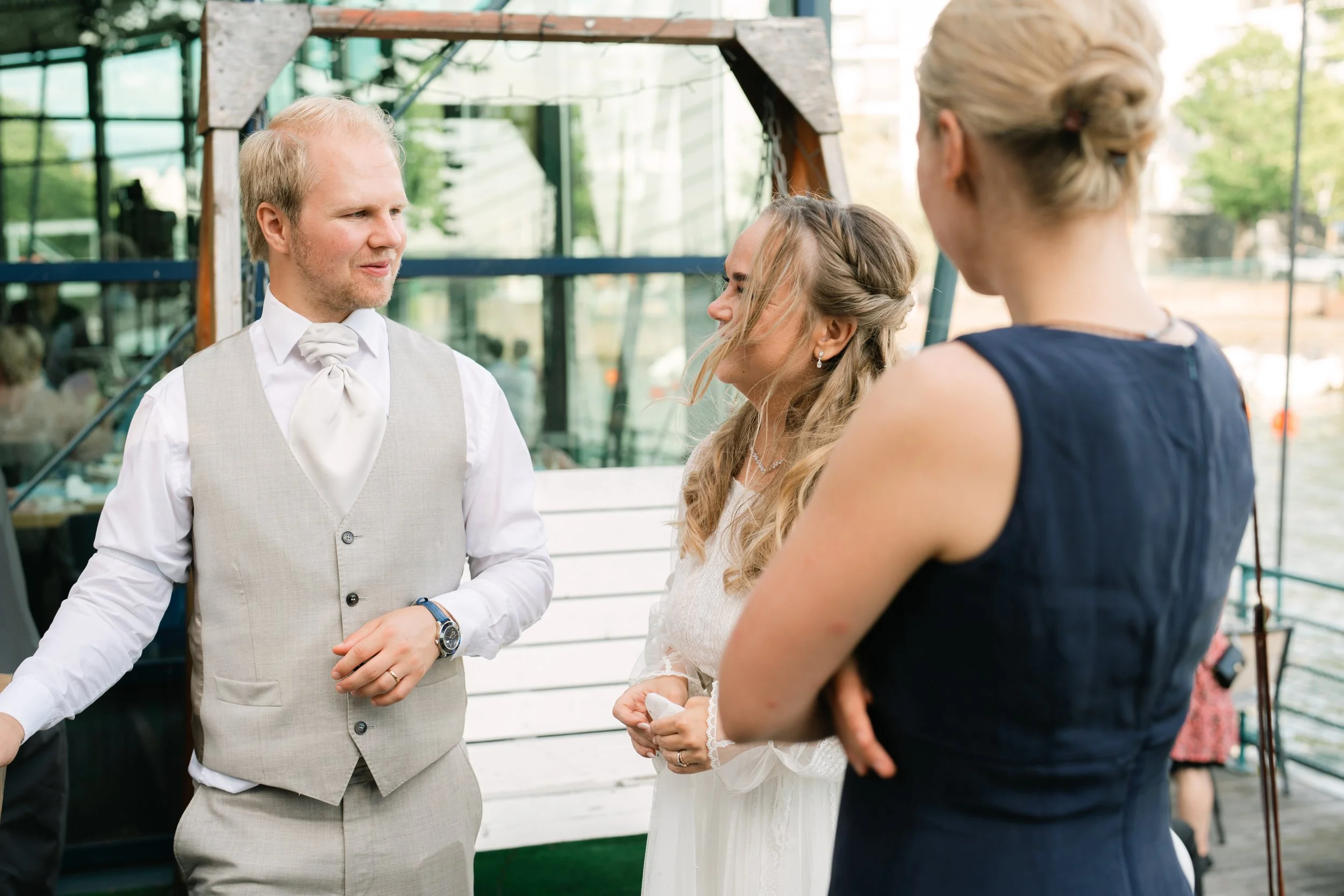 Wedding guests conversing outdoors, man in gray suit and woman in white dress.