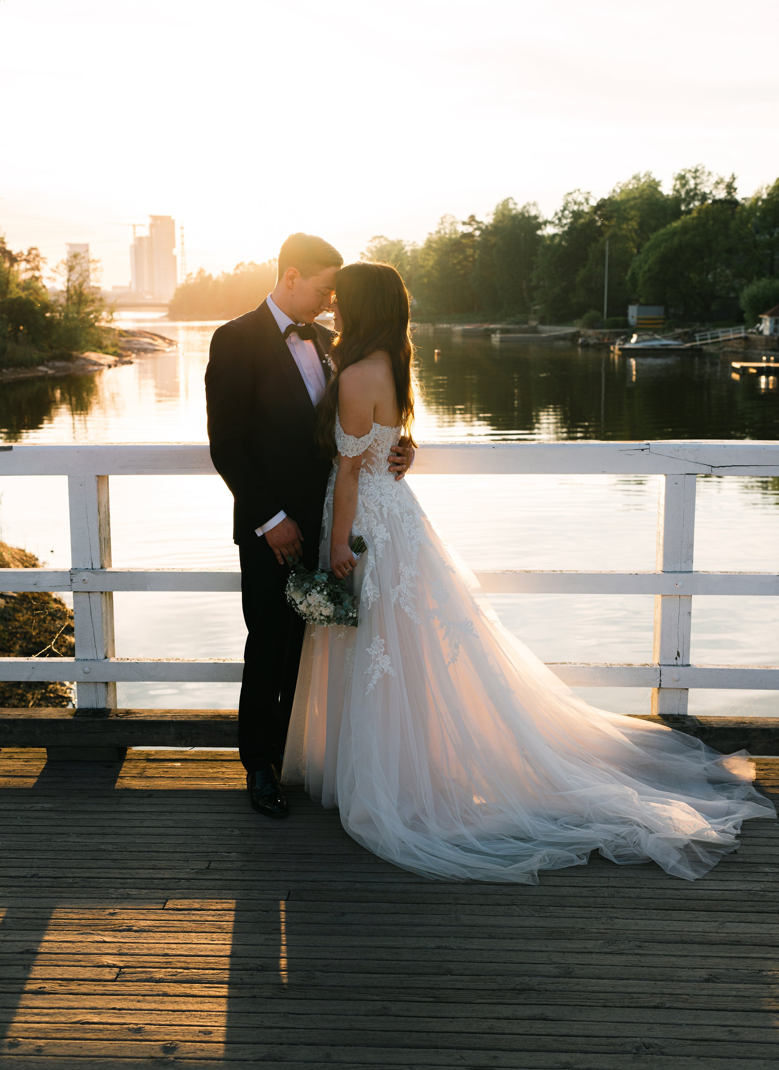 Bride and groom embrace on a wooden pier during sunset.