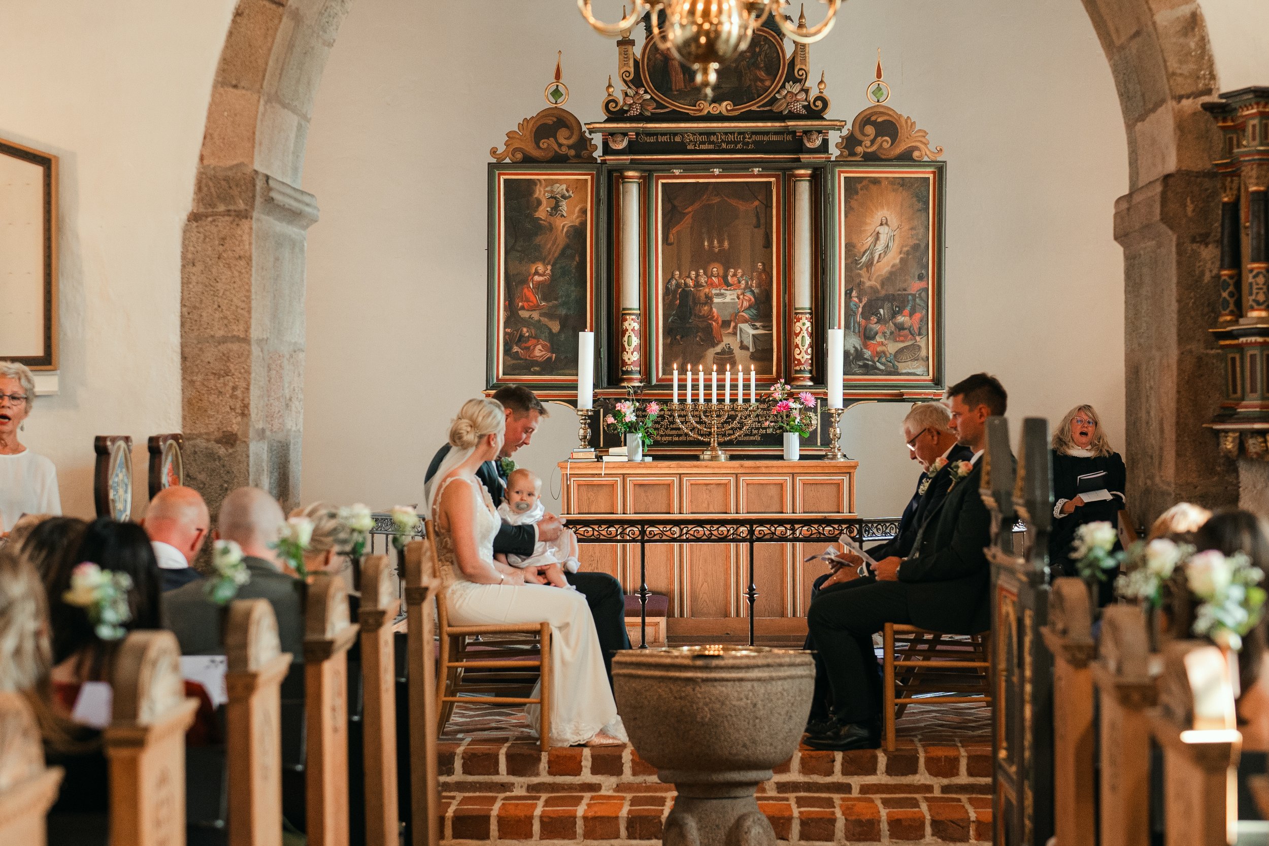 Wedding ceremony in a church with altar, guests seated, and a couple with a child.