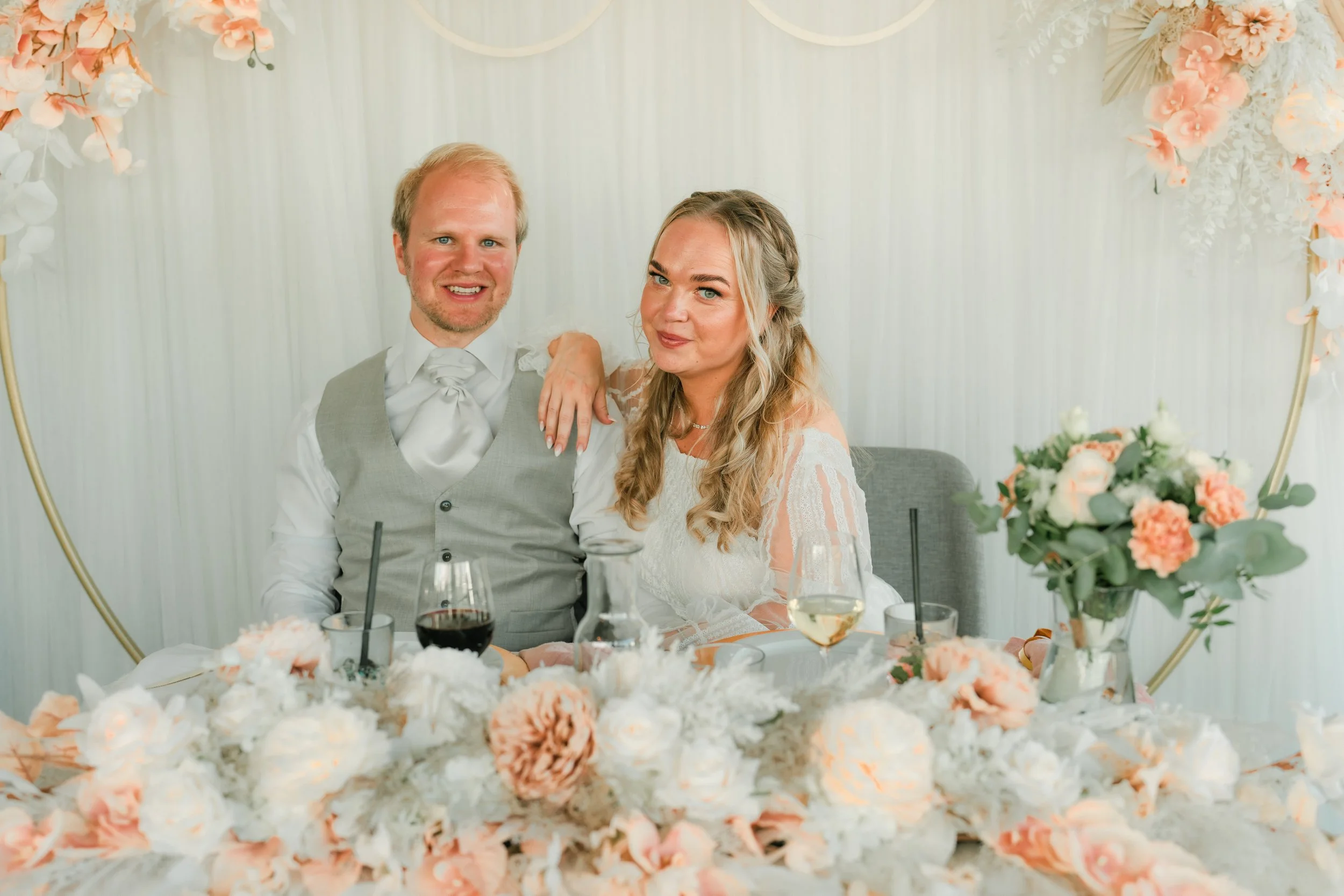 Couple at wedding reception with floral decorations and drinks on table.