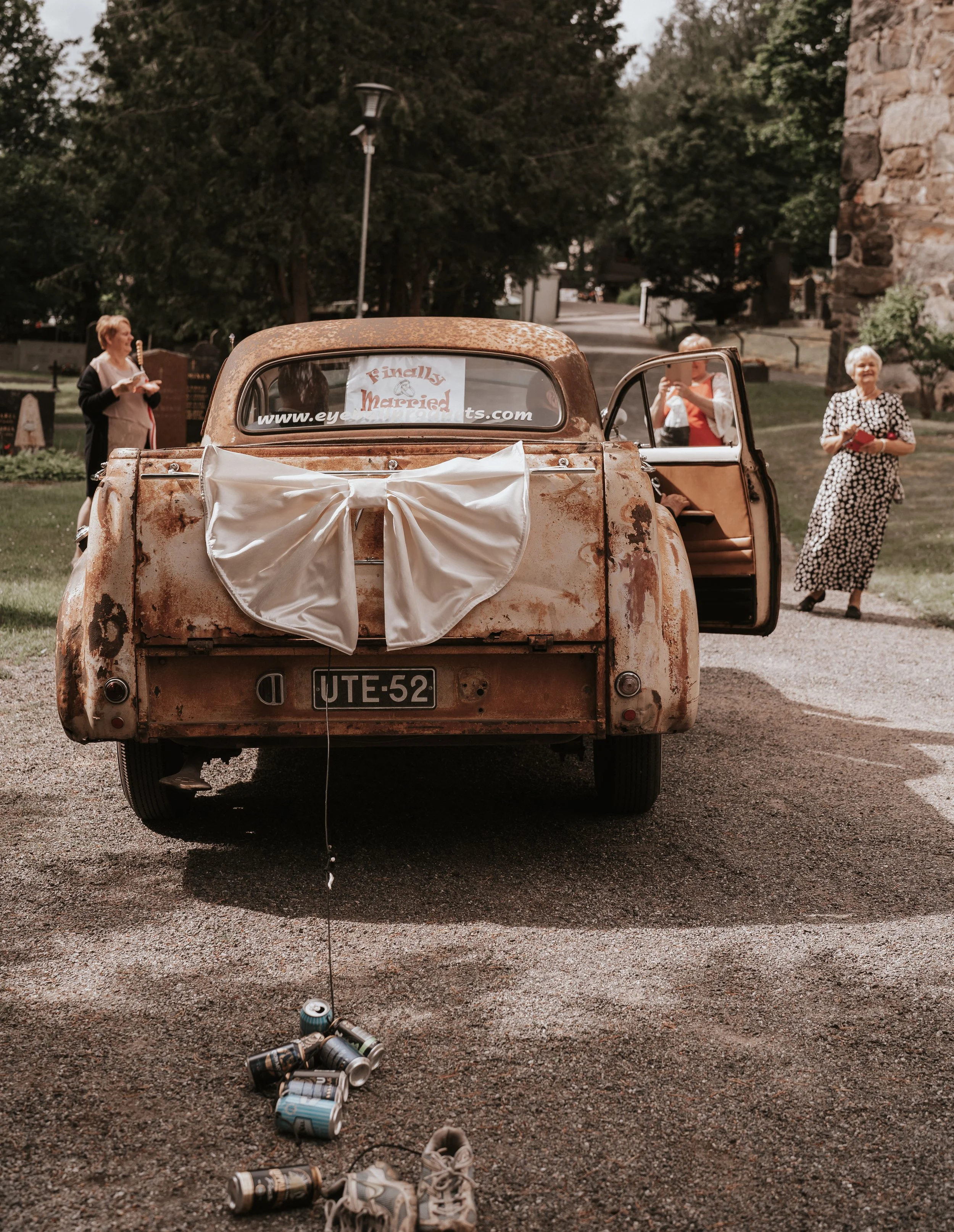 Rustic wedding car with "Finally Married" sign, white bow, and cans tied to bumper.