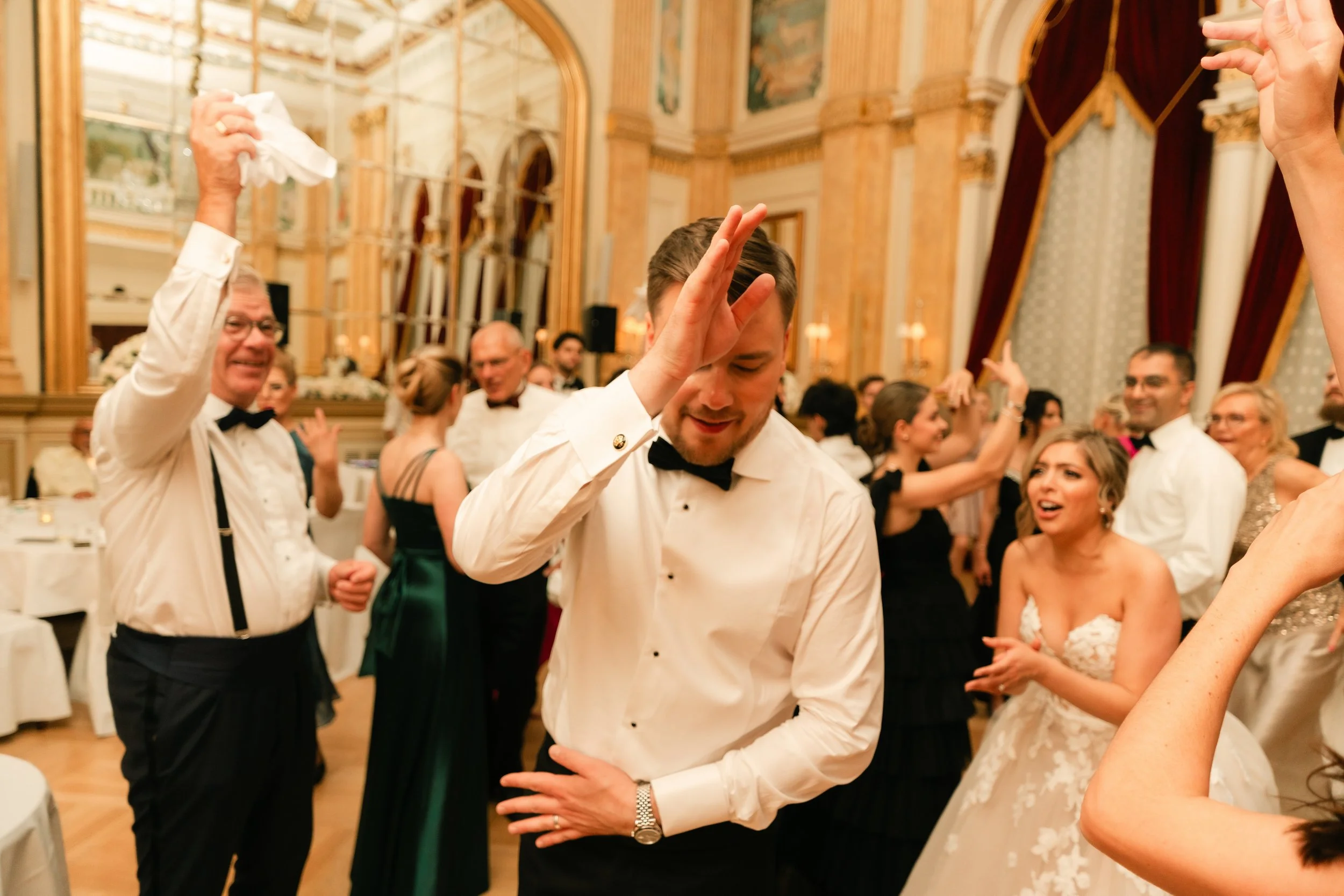 Wedding reception with people dancing in formal attire inside an elegant venue.