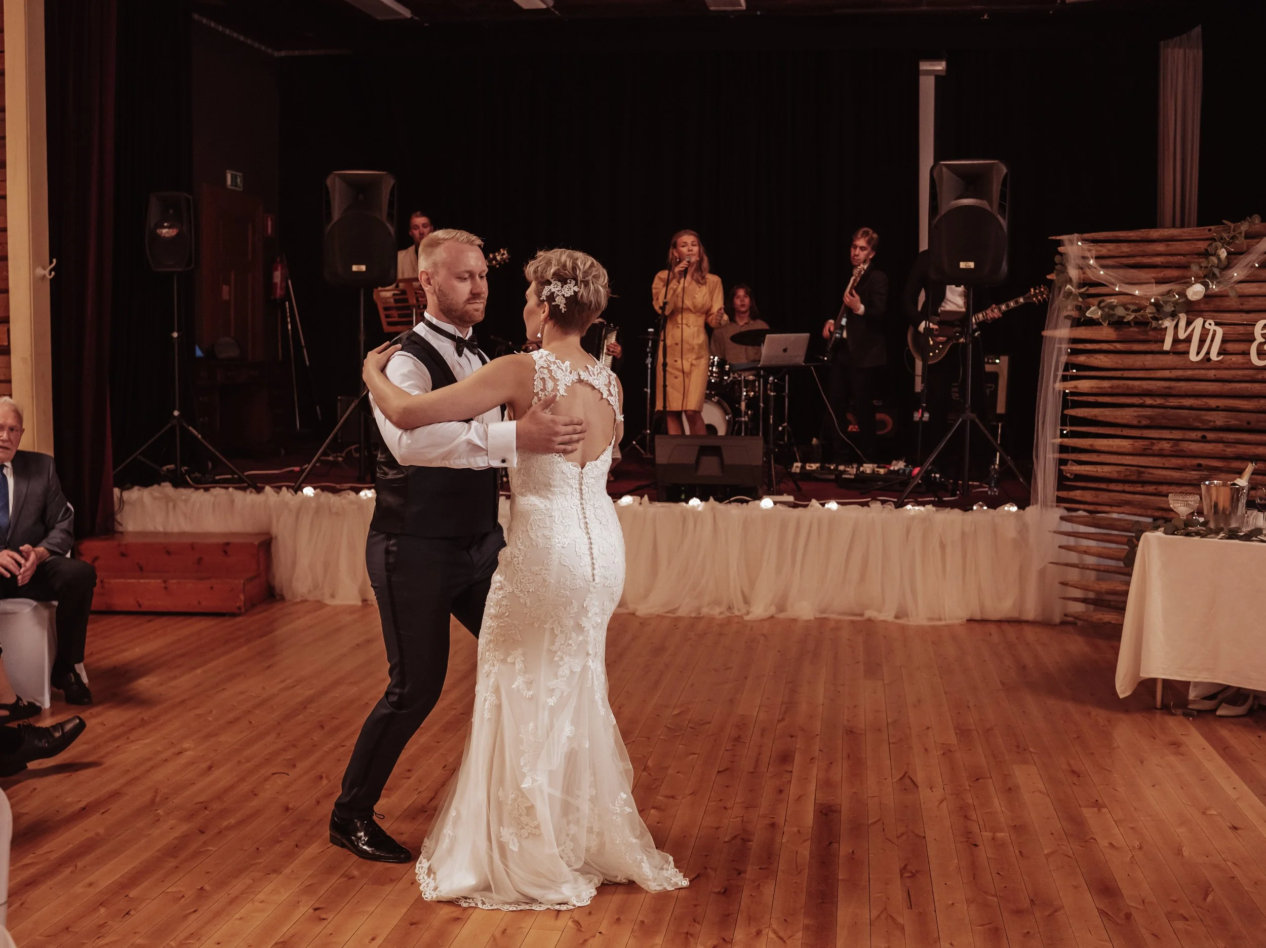 Bride and groom performing first dance at a wedding reception, with live band playing on a stage in the background.