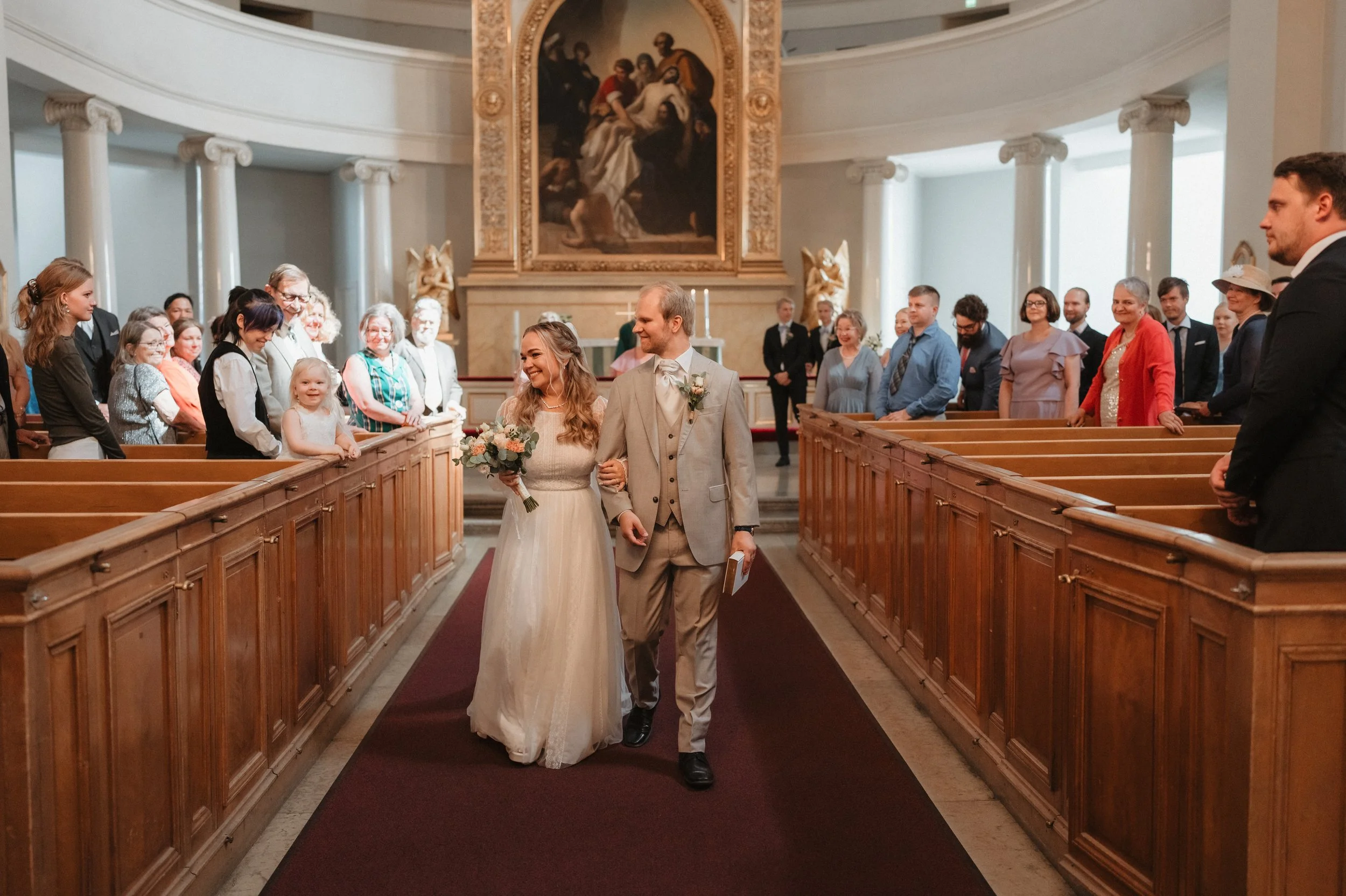 Bride and groom walking down church aisle with guests smiling