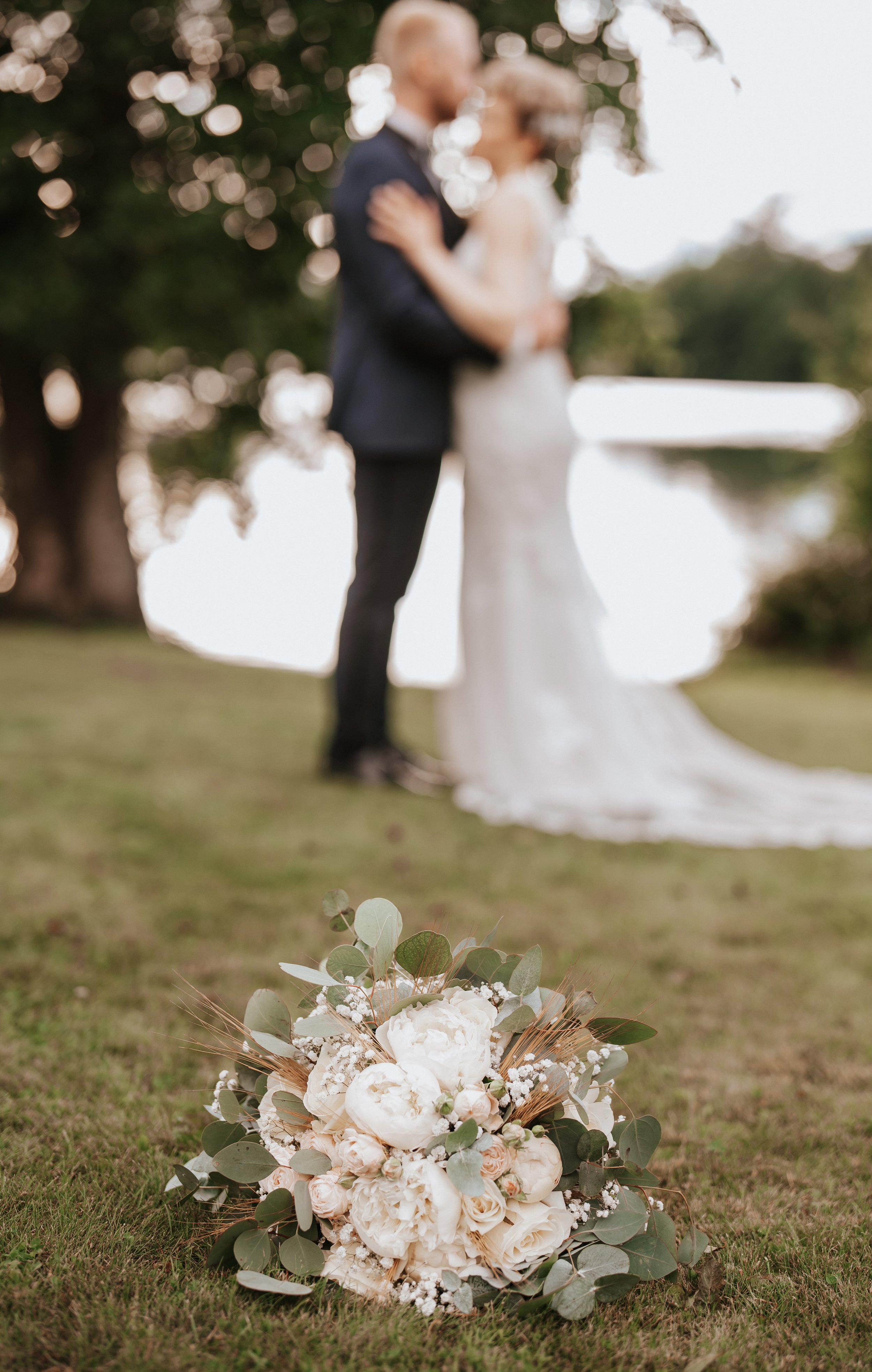 Wedding bouquet on grass with blurred couple in the background.