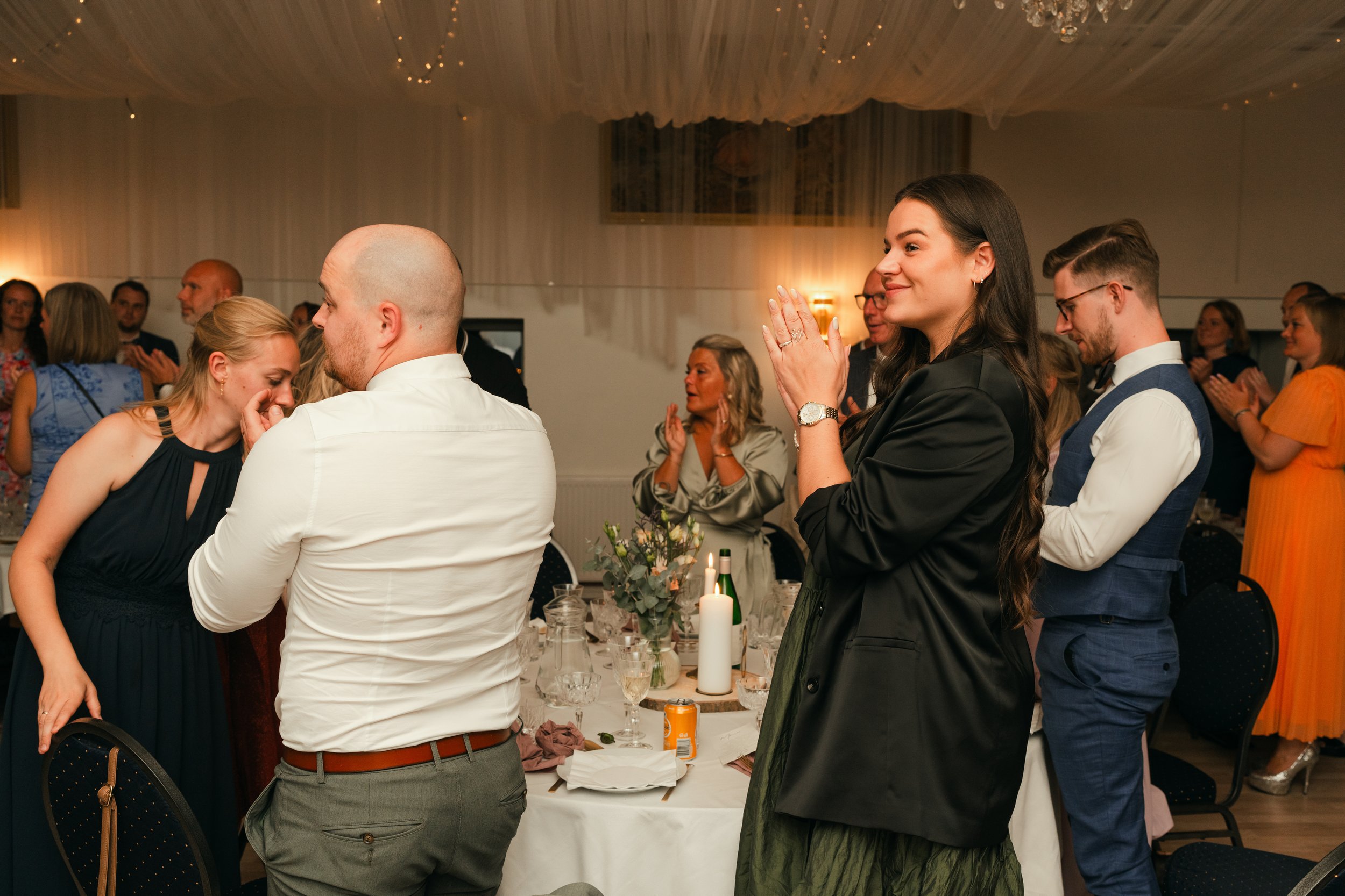 People clapping at an indoor event or celebration with tables set for dining.