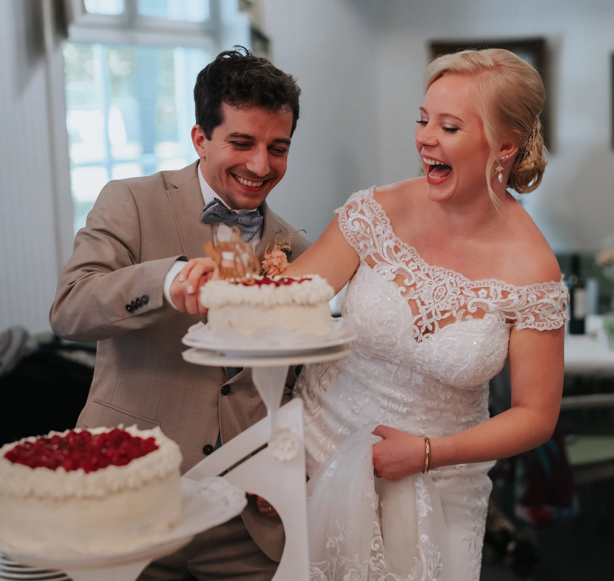 Bride and groom cutting wedding cake, smiling and dressed in a wedding gown and suit.