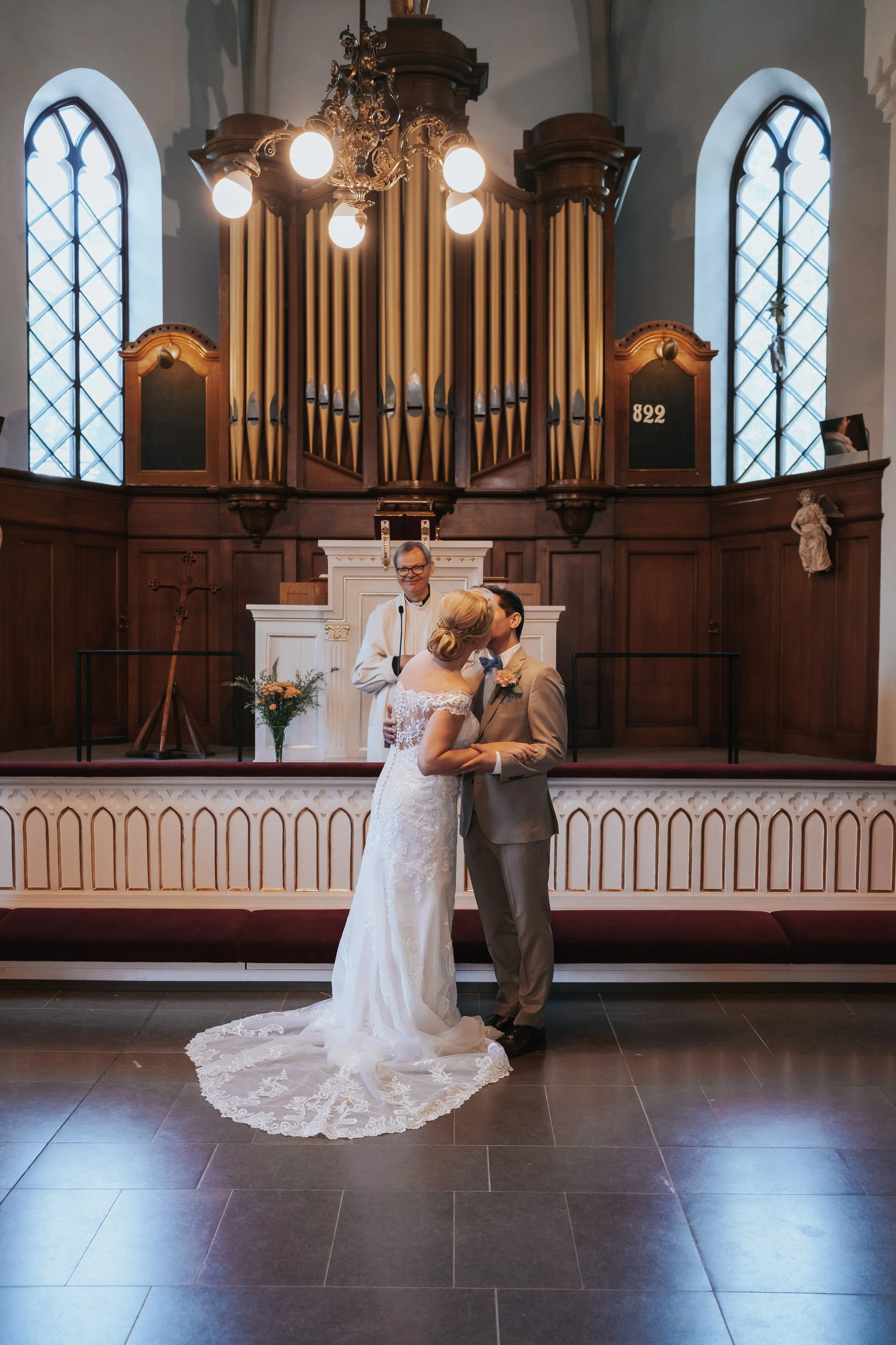 Bride and groom kissing at altar with officiant in church ceremony.