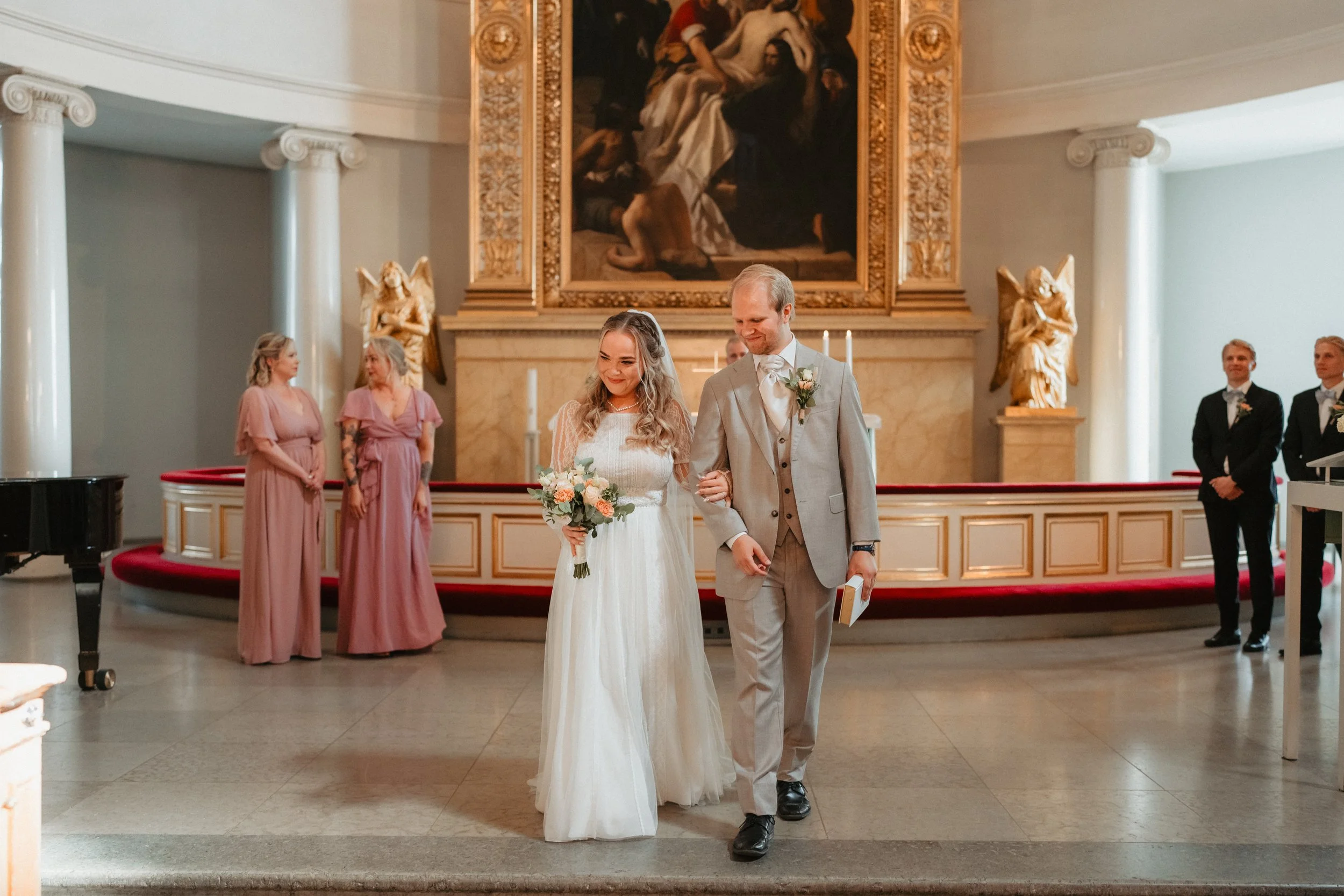 Bride and groom walking down the aisle in a church with bridesmaids in pink dresses and groomsmen in suits, elegant altar background.