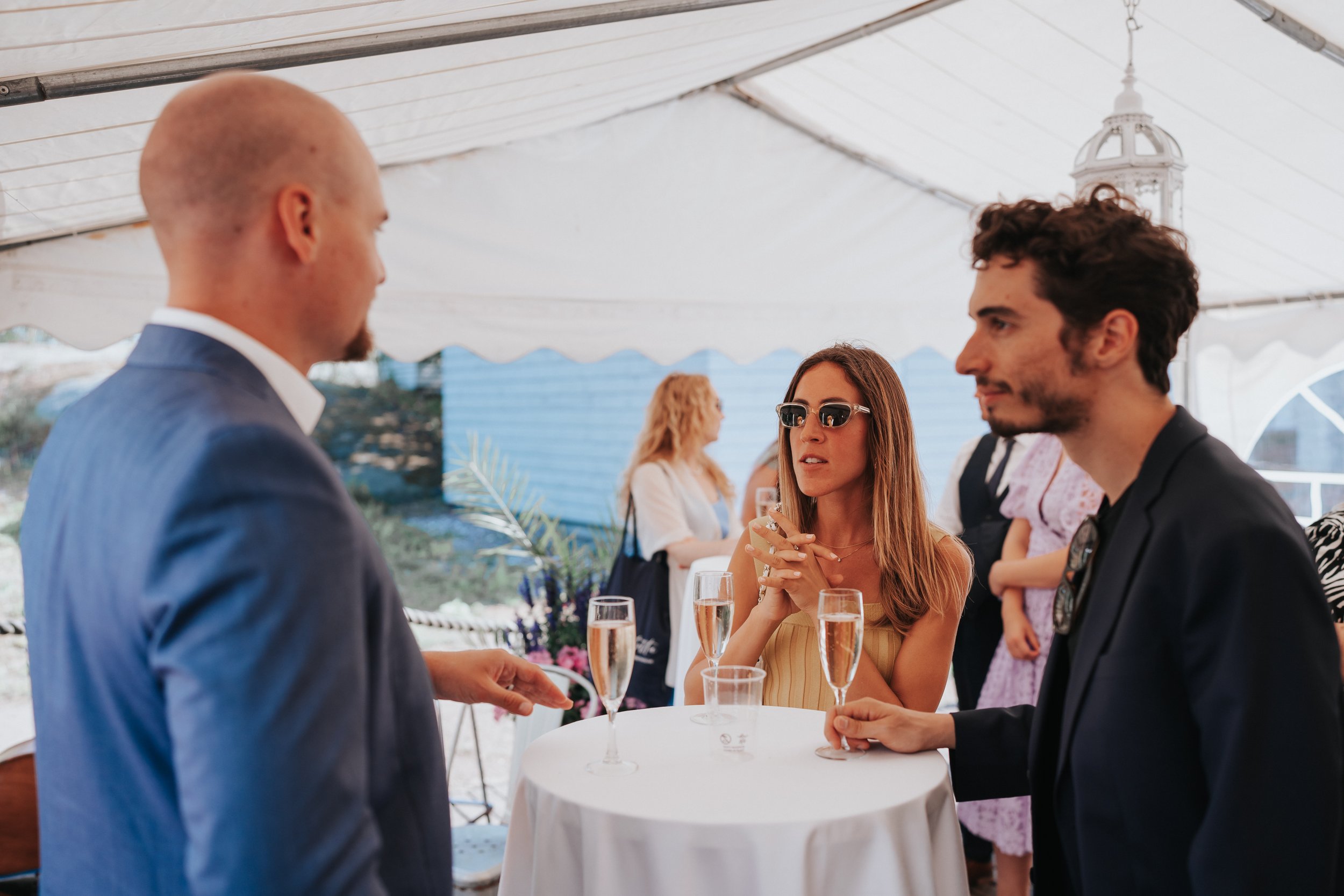 People socializing at an event under a tent, holding champagne glasses.