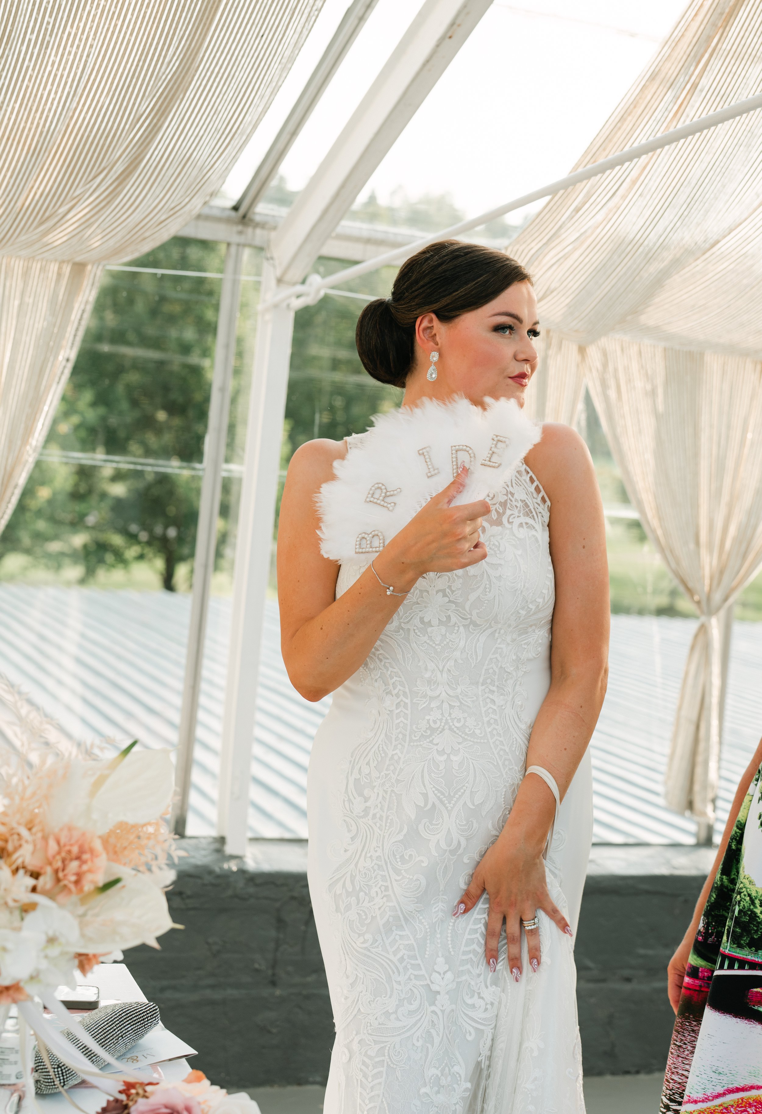 Bride in white lace gown holding a feather fan with "BRIDE" text.